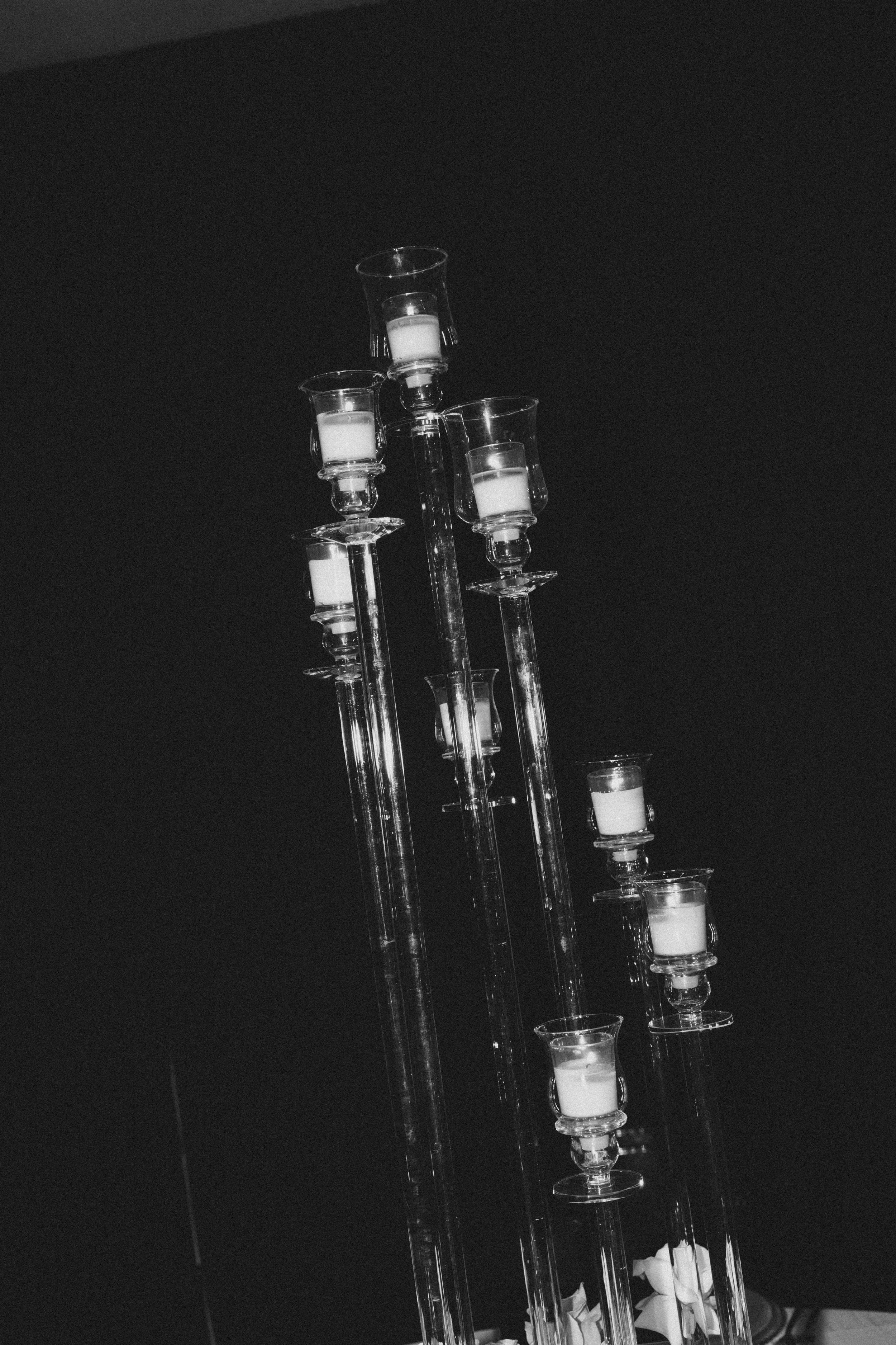 Multiple glass candle holders with white candles inside, set against a dark background.