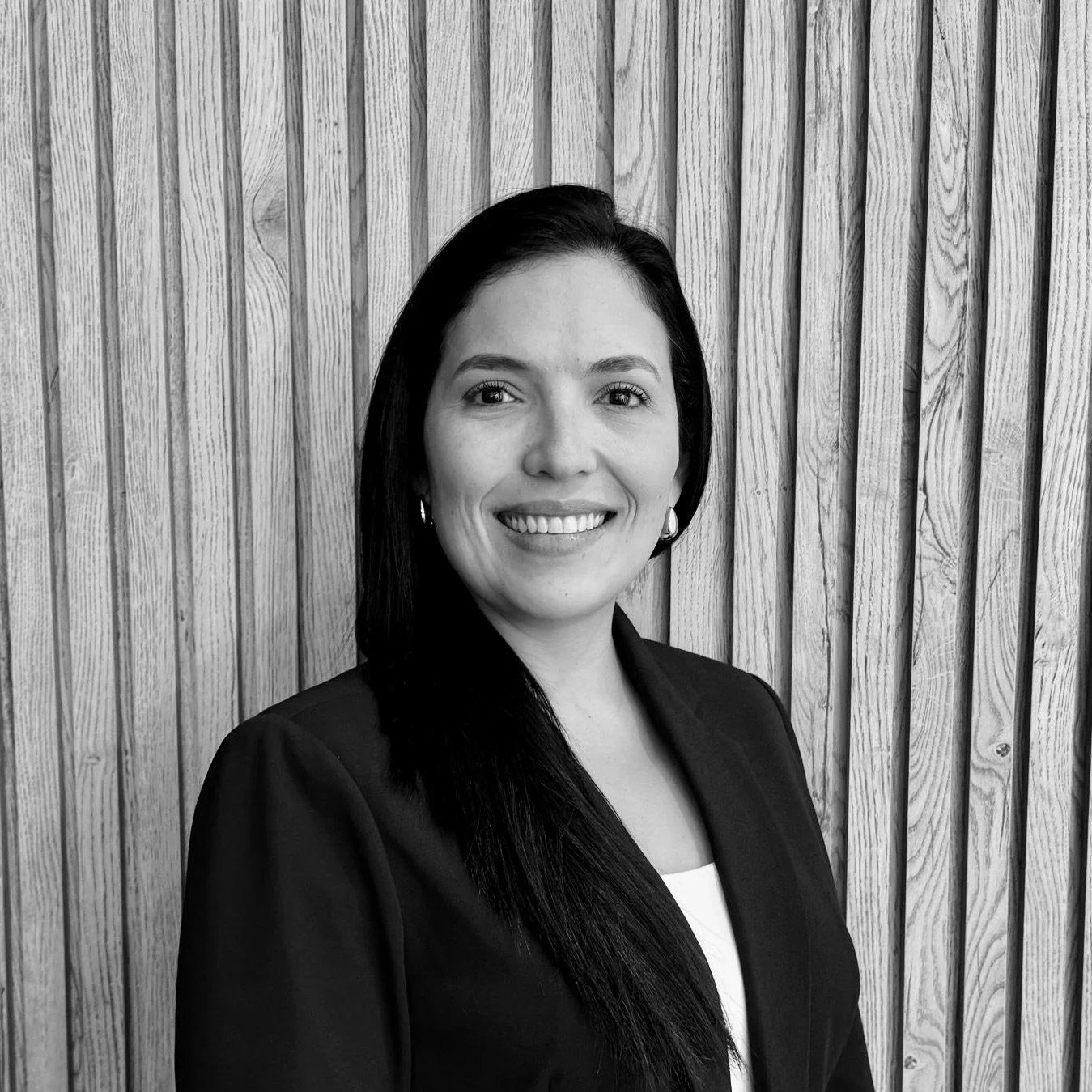 Black and white portrait of a woman smiling, standing in front of a wooden textured wall.