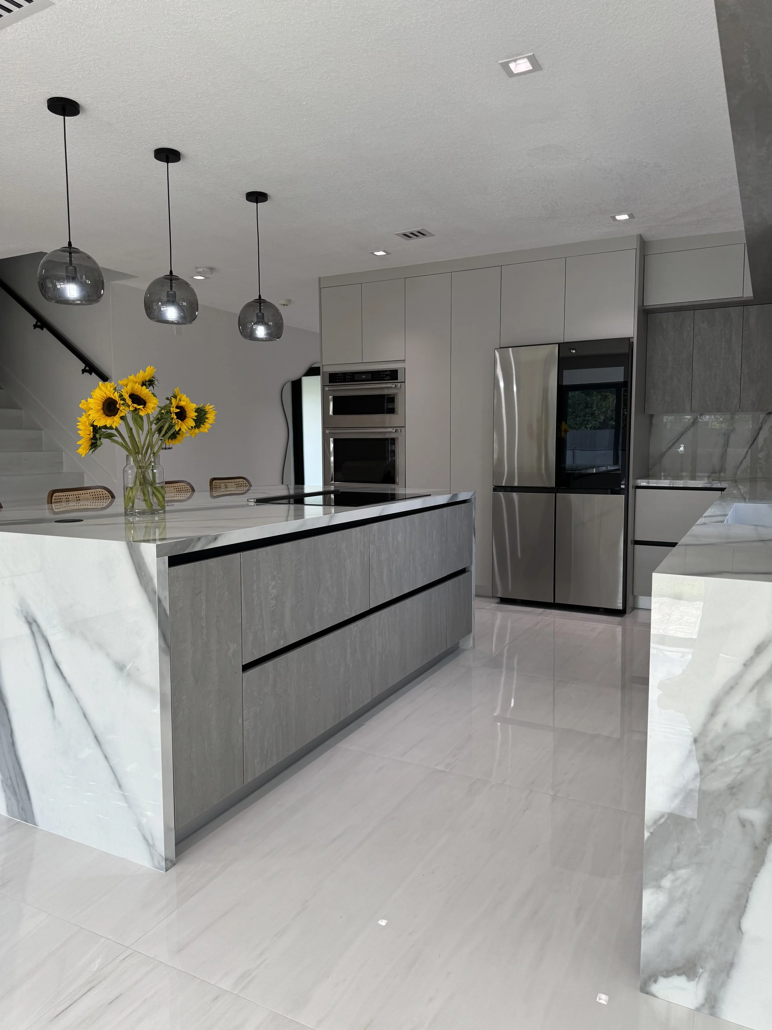 Modern kitchen with porcelain island, stainless steel refrigerator, built-in oven, gray cabinetry.