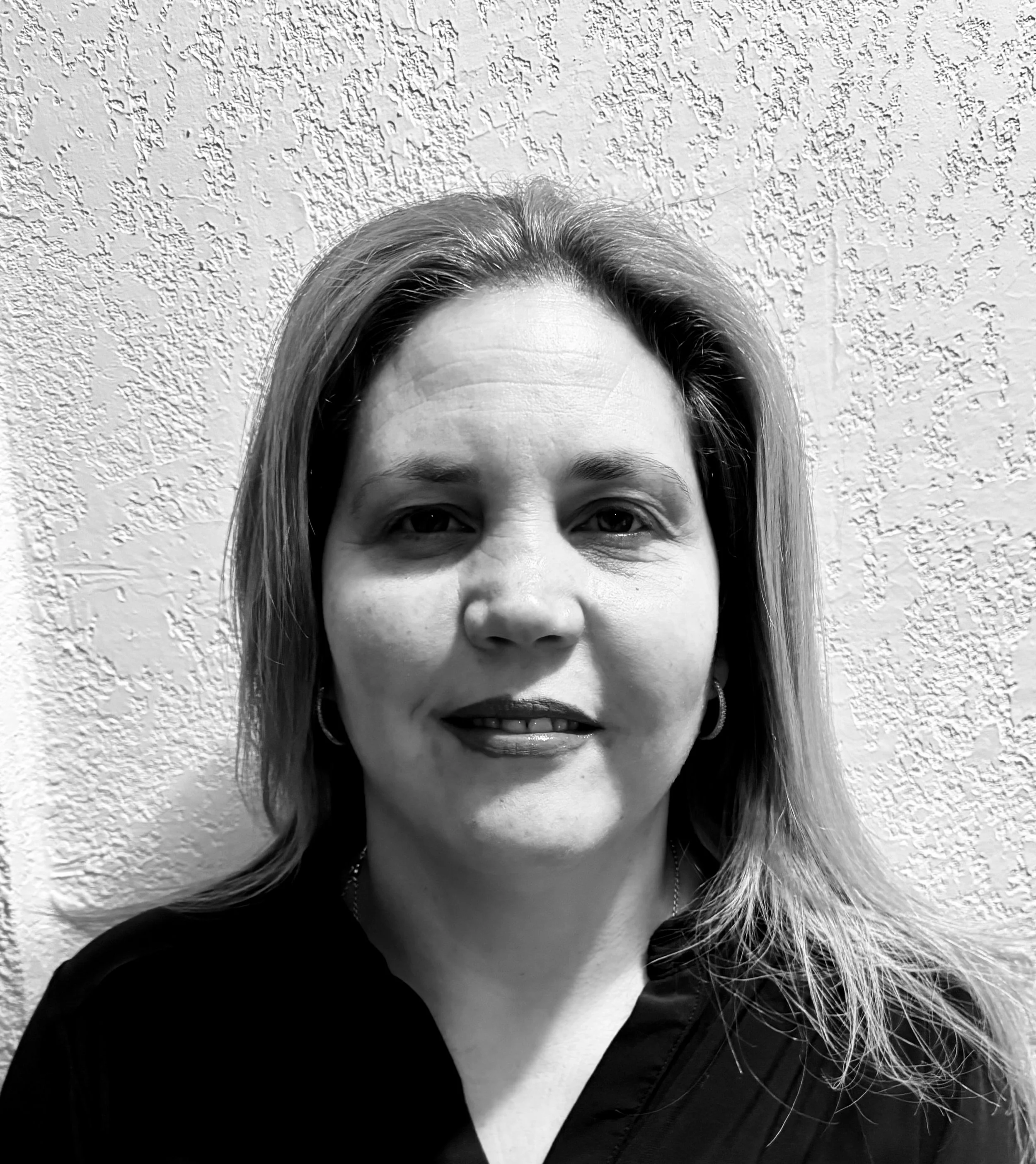 Black and white portrait of a person with long hair against a textured wall.