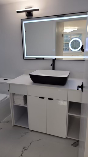 Modern bathroom with a white vanity, black vessel sink, wall-mounted faucet, large illuminated mirror, and neatly stacked towels. Minimalist design with a marble floor.