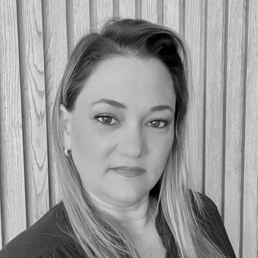 Black and white portrait of a woman with long hair, wearing a dark top, against a wooden panel background.