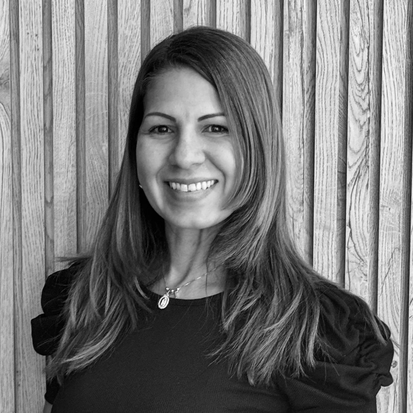 Smiling woman with long hair standing in front of a wooden slatted wall.