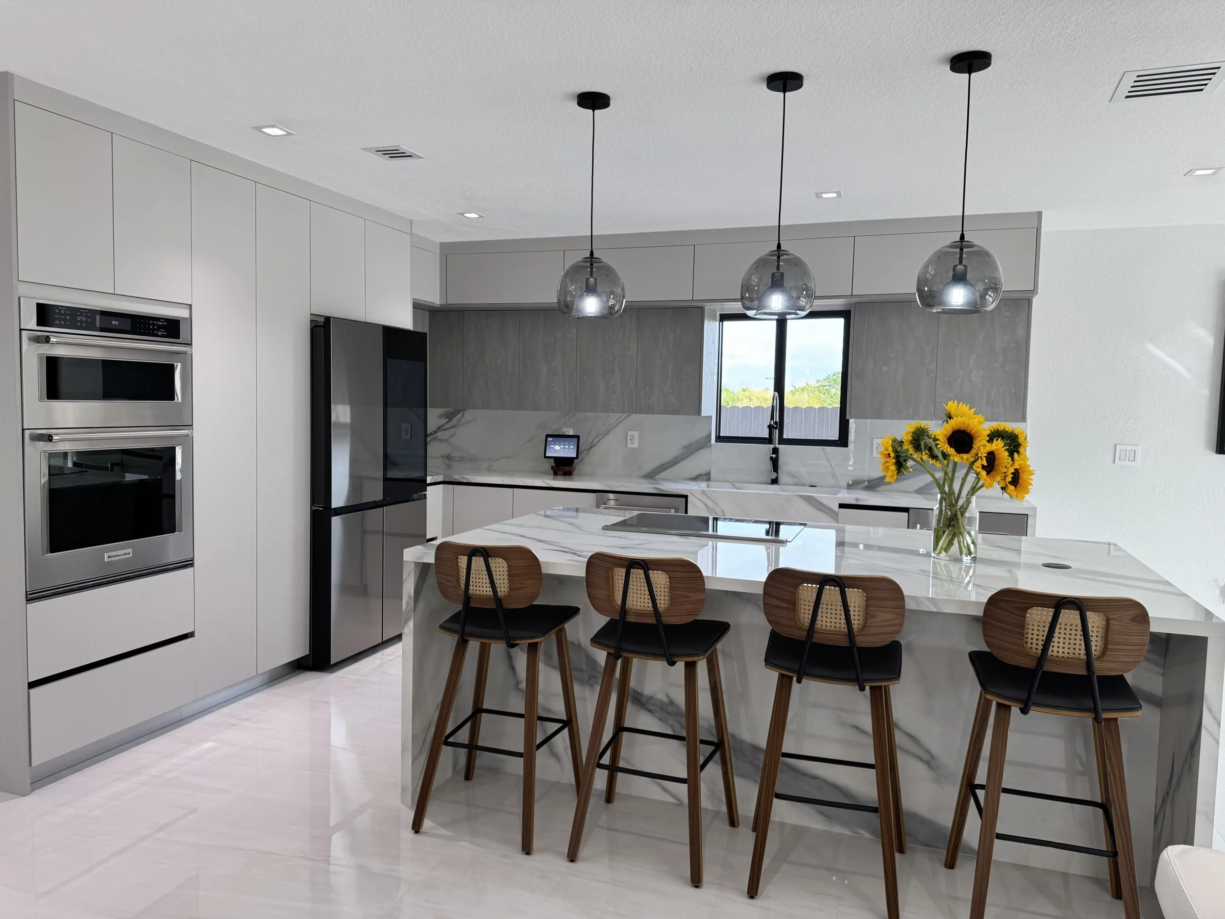 Modern kitchen with gray cabinets, stainless steel appliances, porcelain island with four wooden barstools, gray upper cabinets, black faucet.