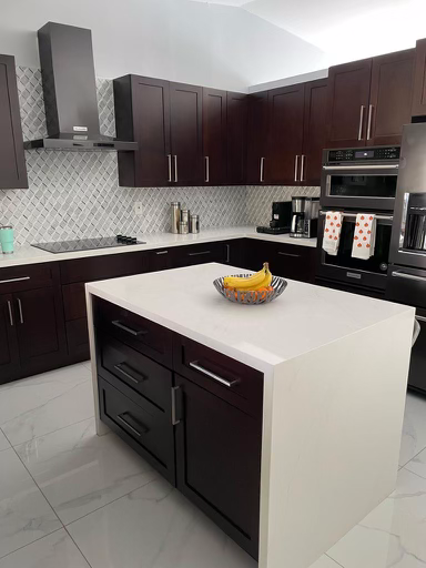 Modern kitchen with dark wood cabinets, stainless steel appliances, white countertops, kitchen island, and a bowl of bananas.
