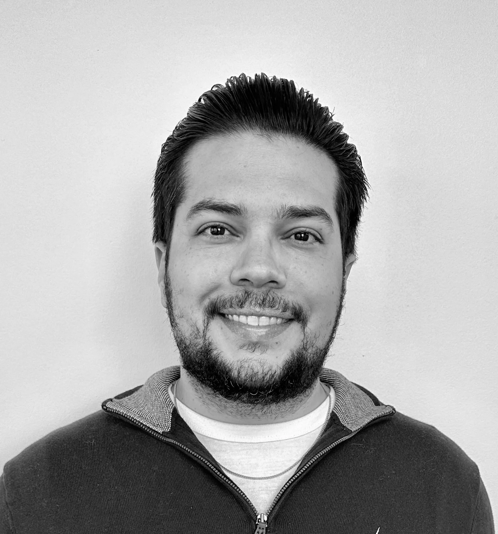 Black and white portrait of a smiling man wearing a collared jacket and t-shirt.