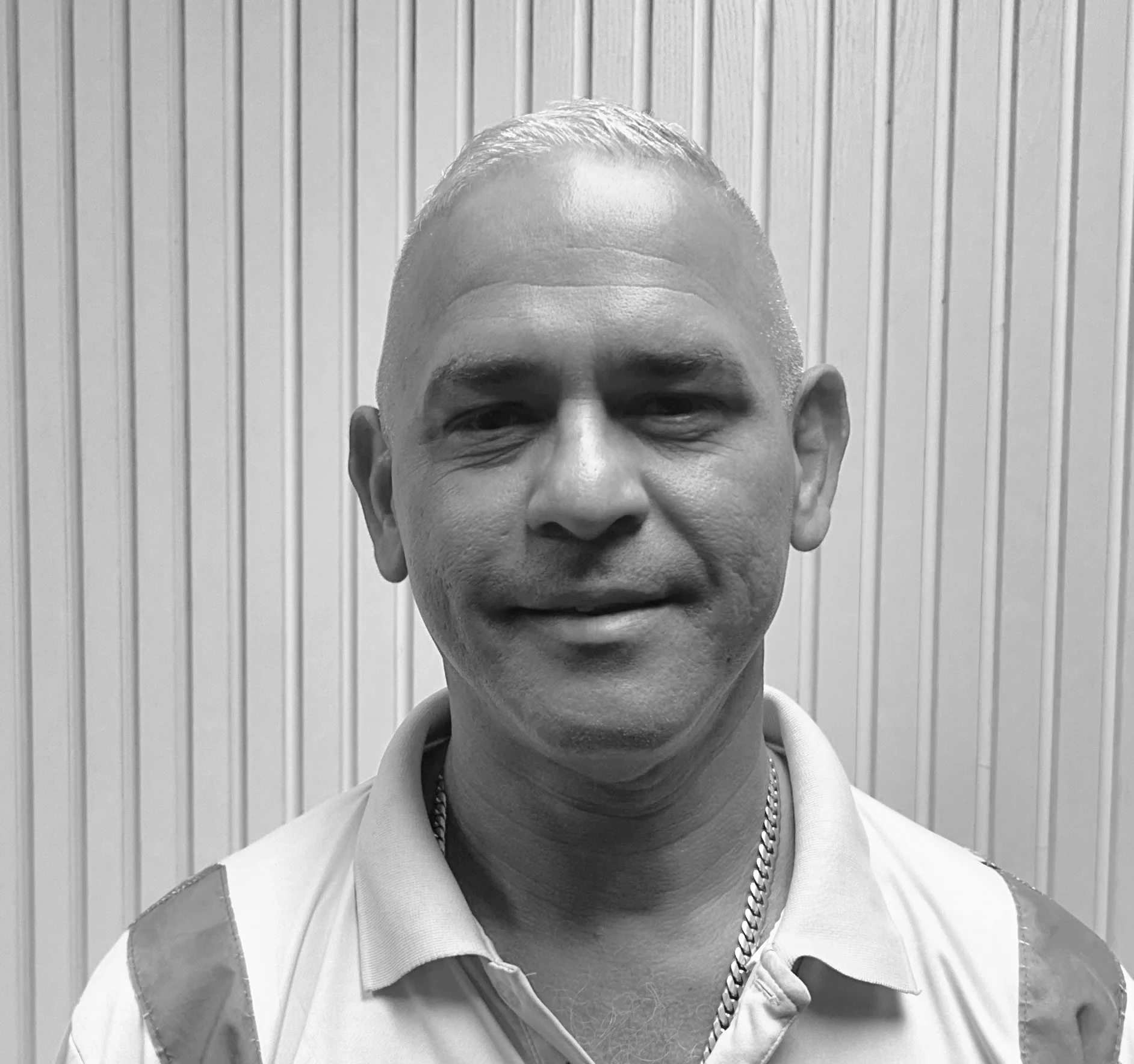 Black and white portrait of a man in a collared shirt in front of a striped wall.