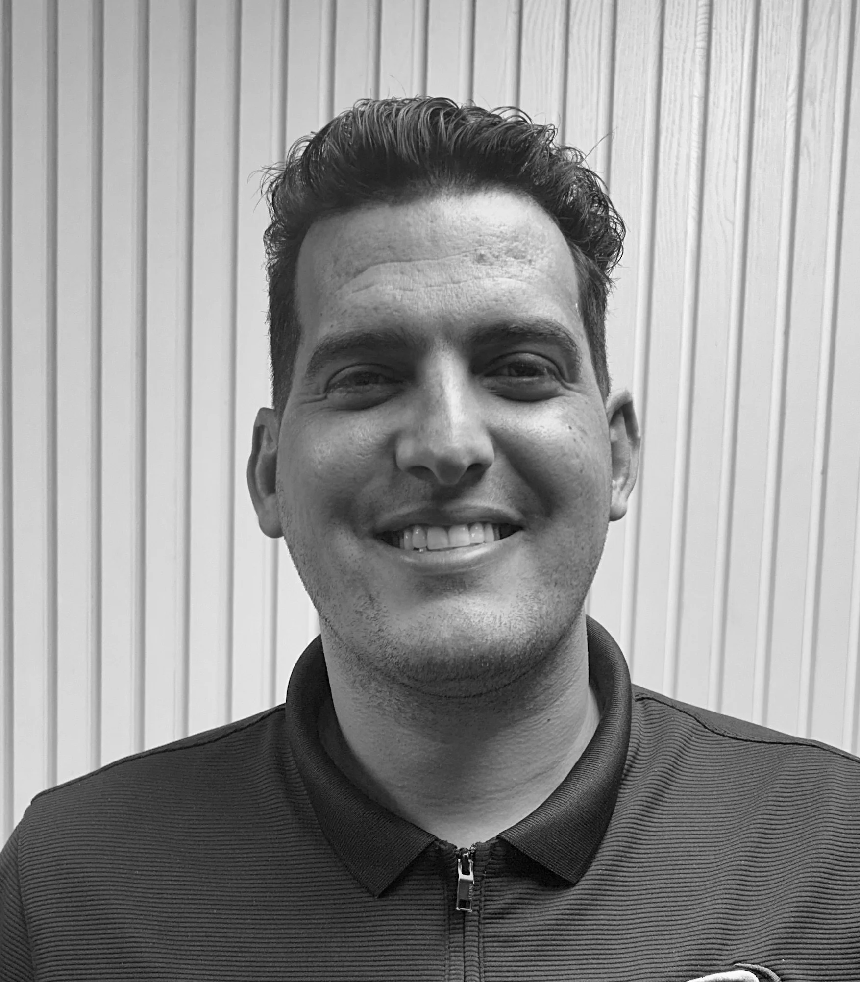 Black and white portrait of a man smiling in front of a striped wall.