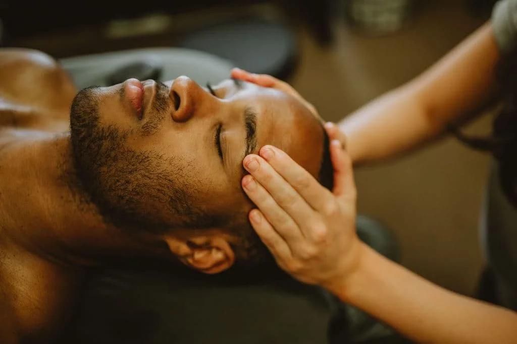 black, male client lying on their back receiving gentle hands-on cranial sacral therapy for headaches from a licensed provider at The Studios at Summit in centennial, colorado