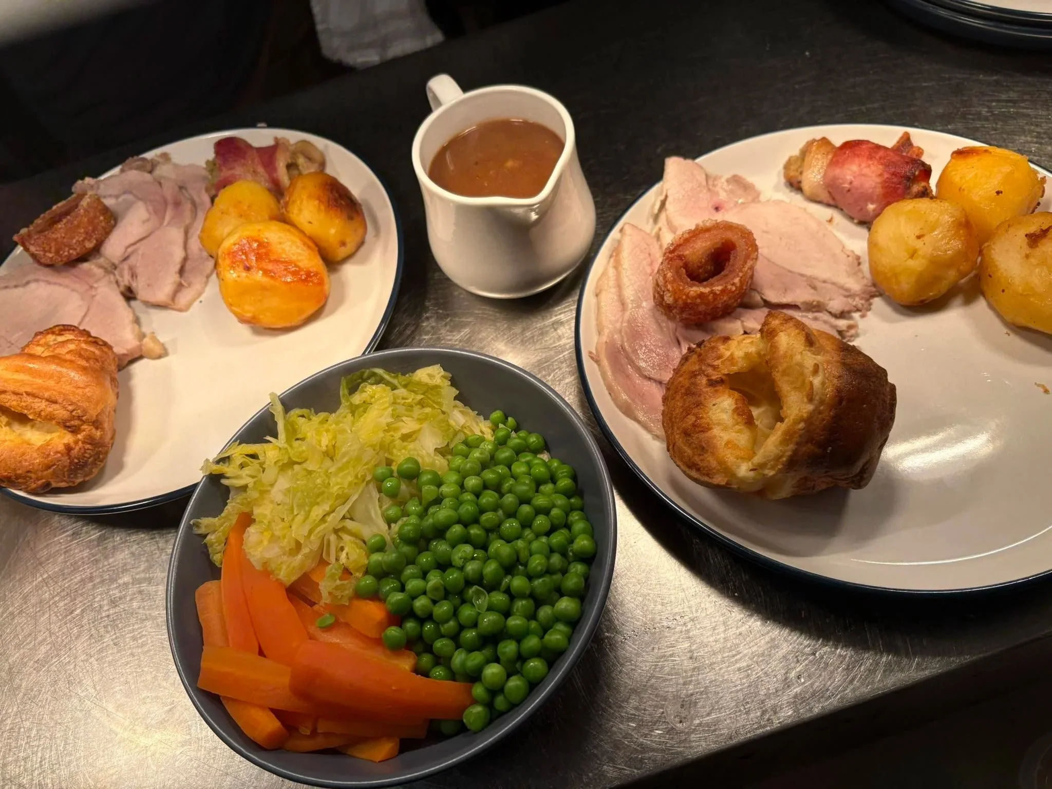 A plate of roast meat, potatoes, and a cup of gravy, with a separate bowl of mixed vegetables including carrots, peas, and shredded lettuce.