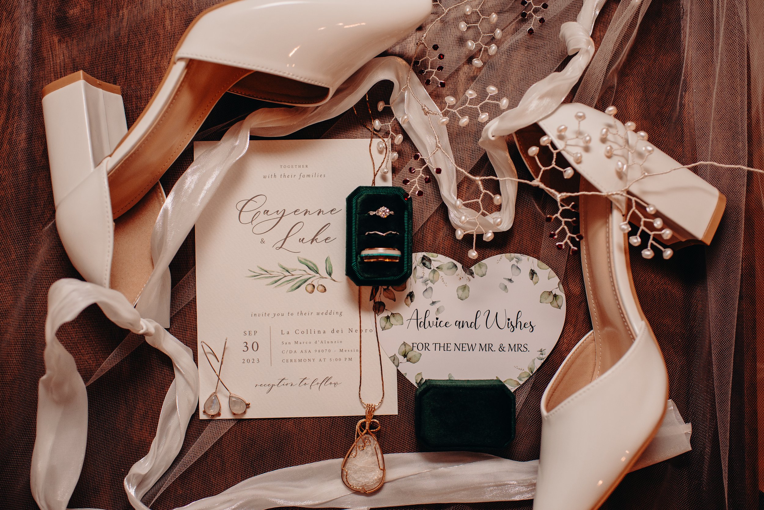 Wedding invitation, bridal shoes, jewelry, and accessories arranged on a maroon fabric with ribbons and decorative elements.
