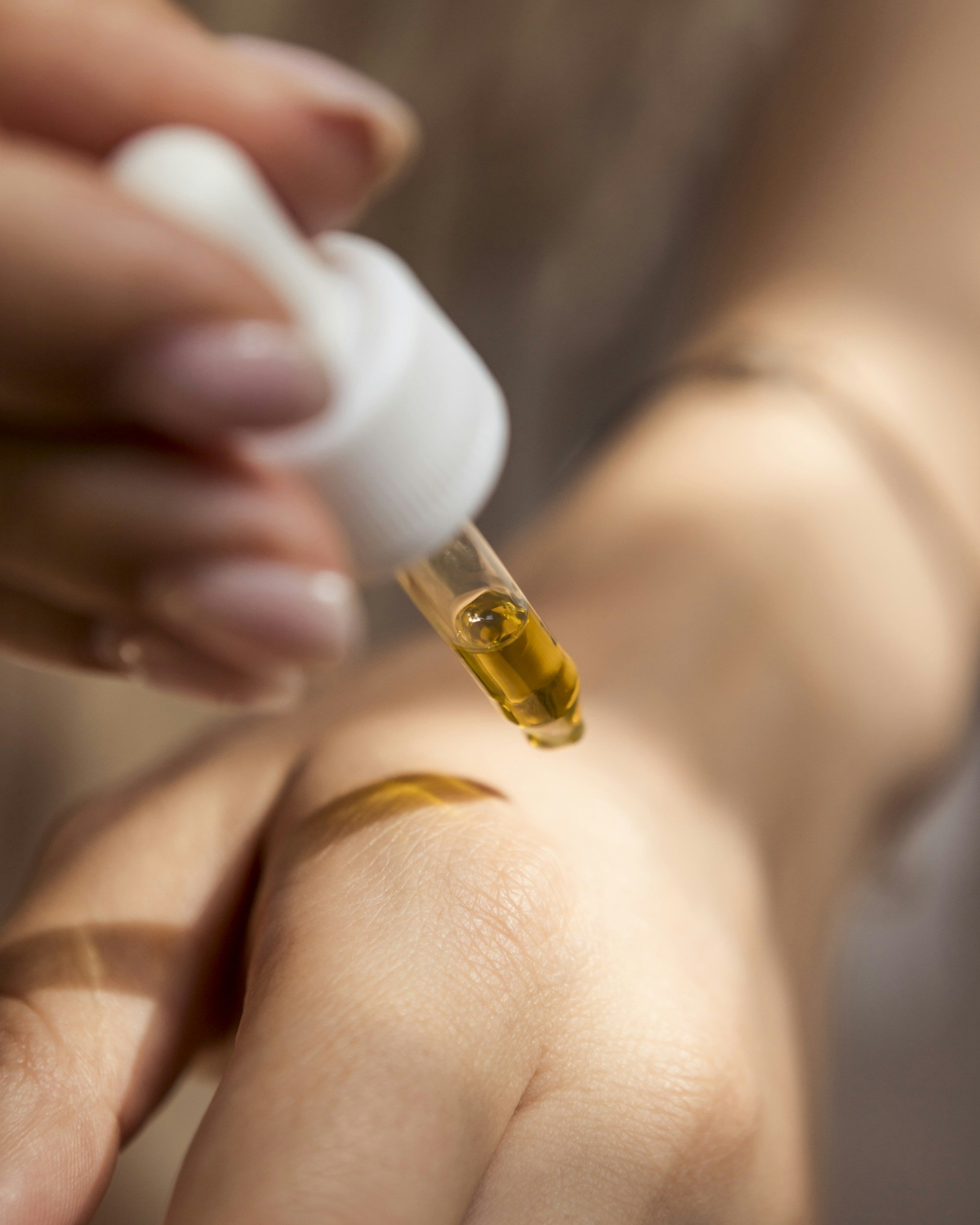 Close-up of a person applying a dropper of golden liquid onto skin.