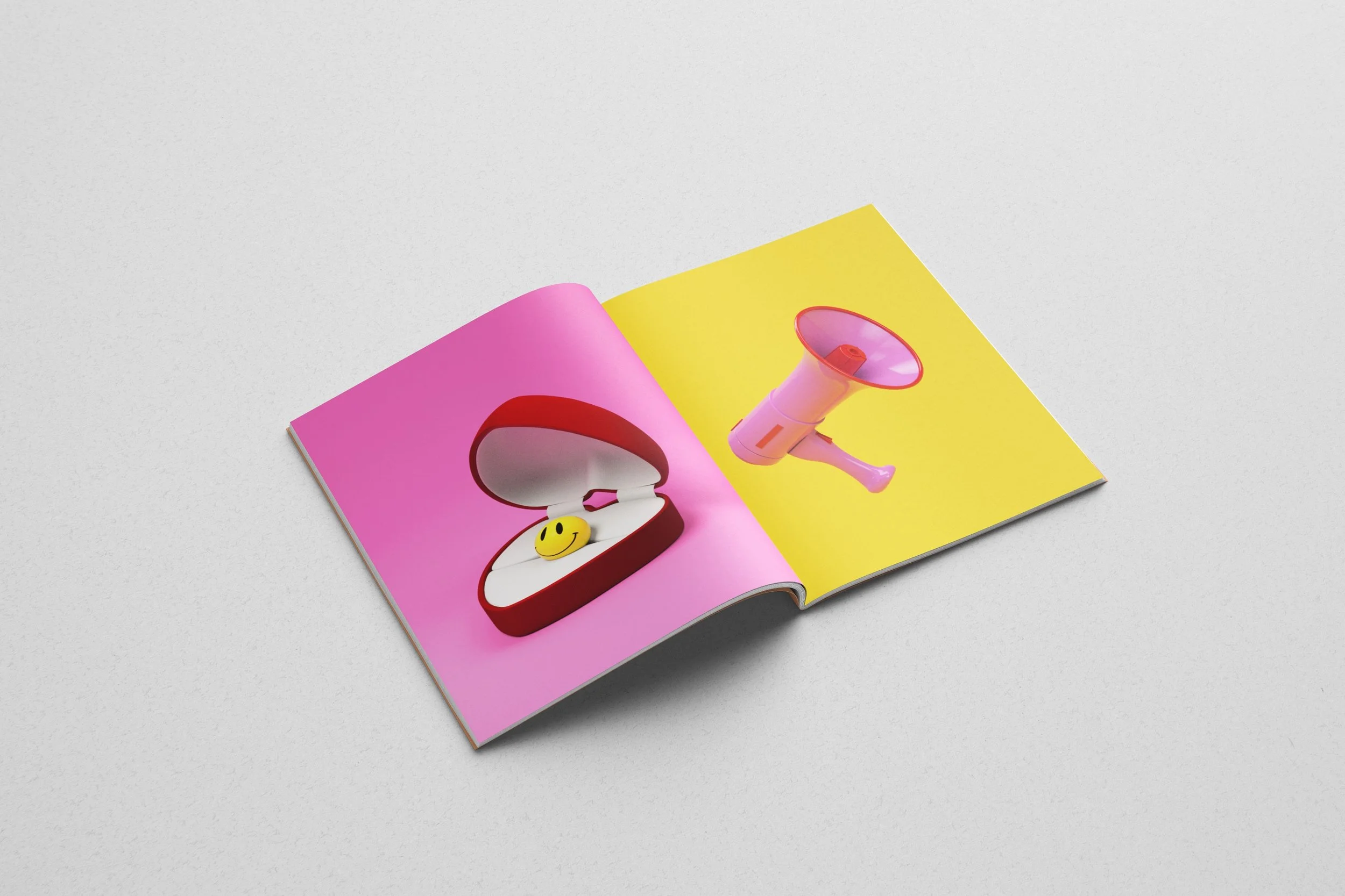 Open magazine featuring a pink and red jewelry box with a yellow smiley face inside on the left page, and a pink megaphone on a yellow background on the right page.