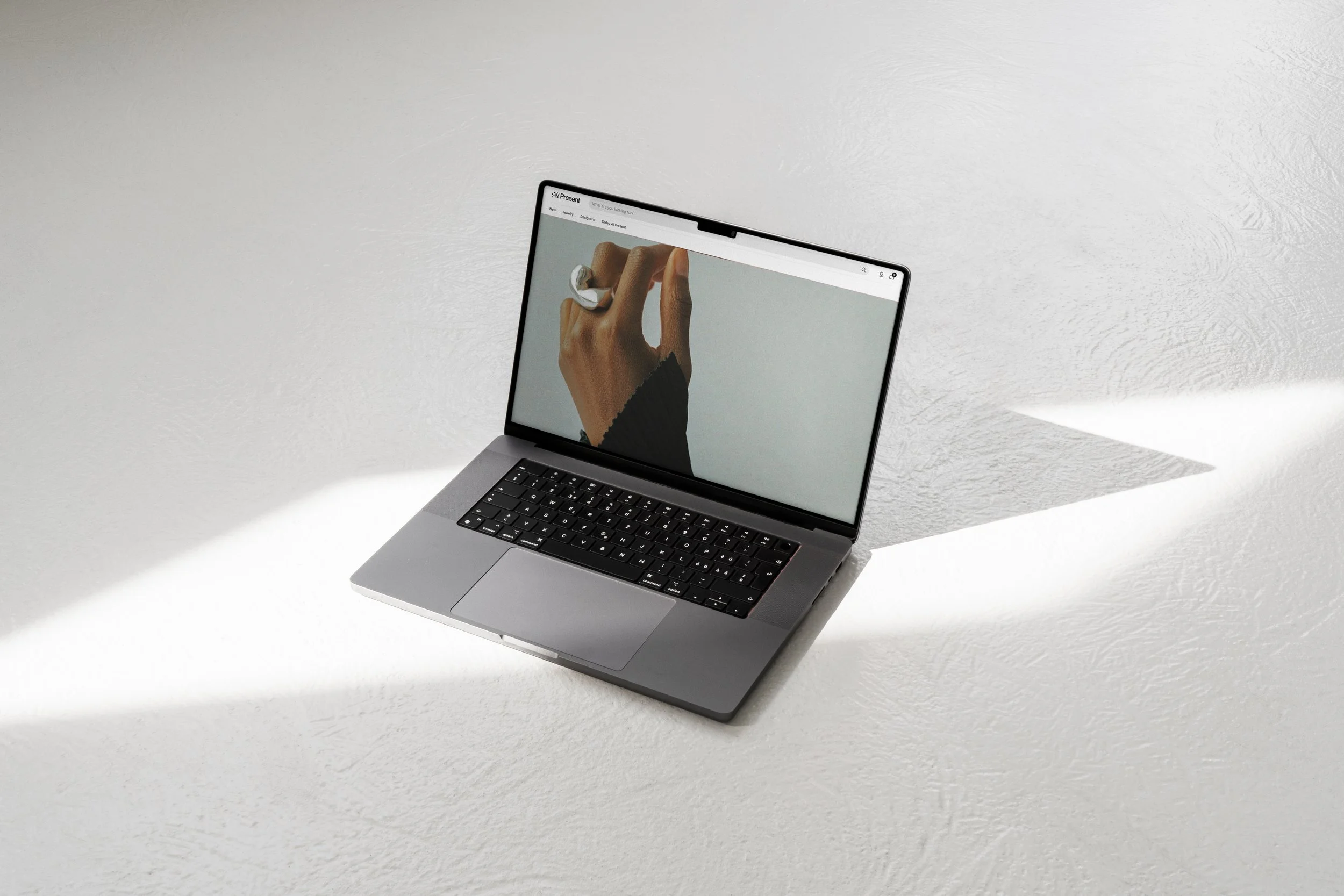 A laptop on a white textured surface displaying a hand with rings on its finger on the screen.