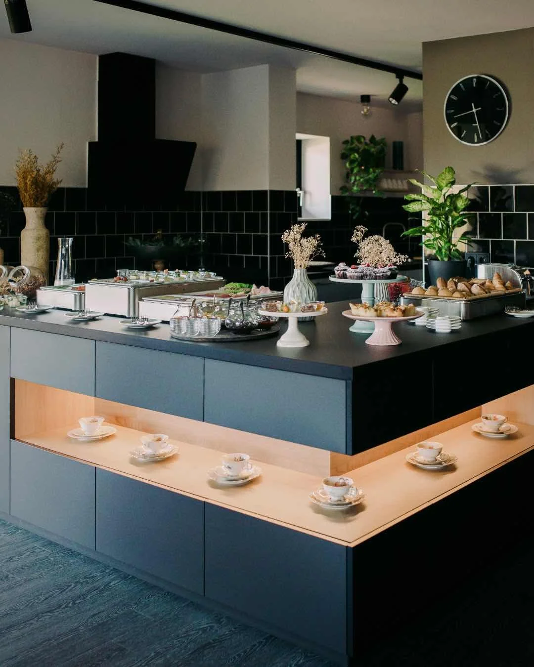 Ein modern gedeckter Frühstückstresen mit Tassen, Deko-Vasen, Blumen und Gebäck in einem häuslichen Esszimmer.