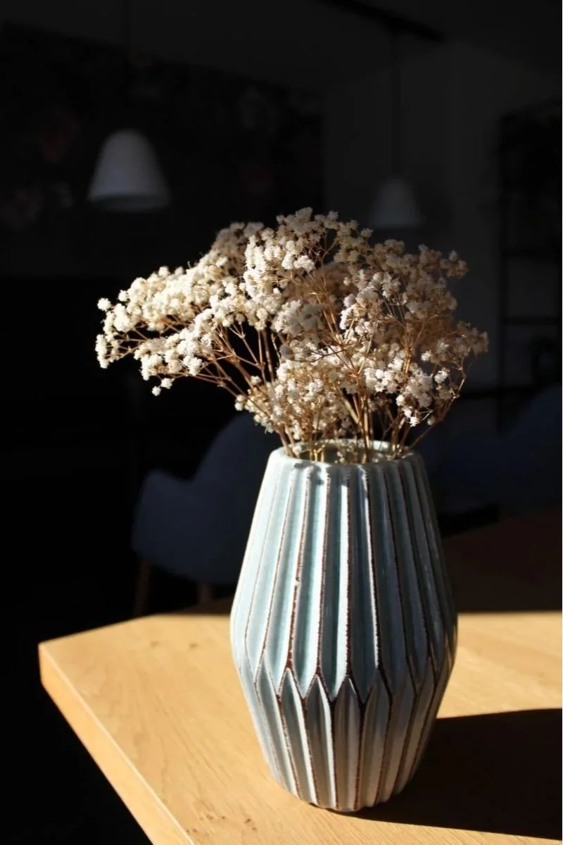 Weiße Trockenblumen in einer silbernen Vase auf einem Holztisch bei Sonnenlicht