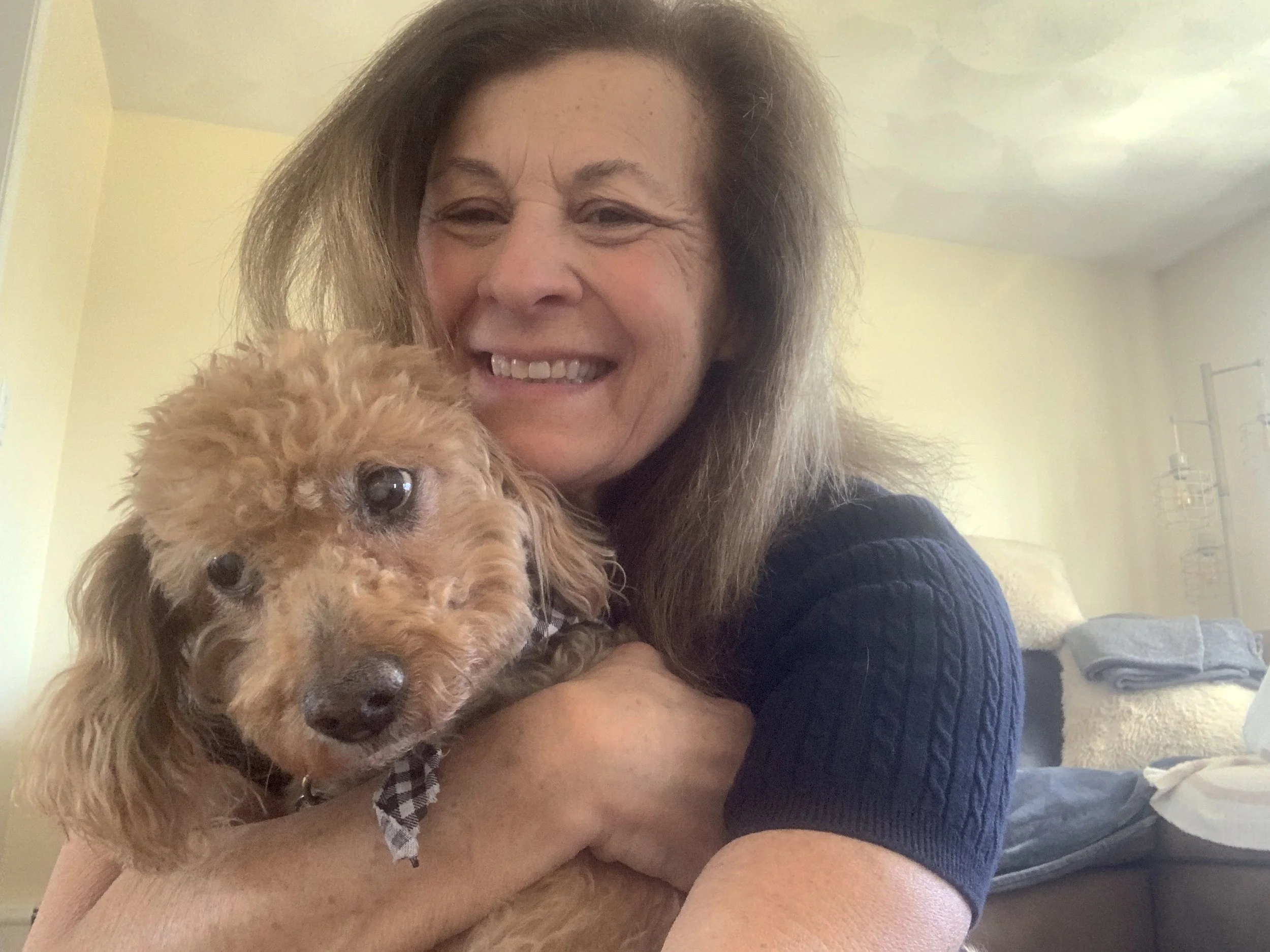 Smiling woman cuddling a small, curly-haired dog indoors.