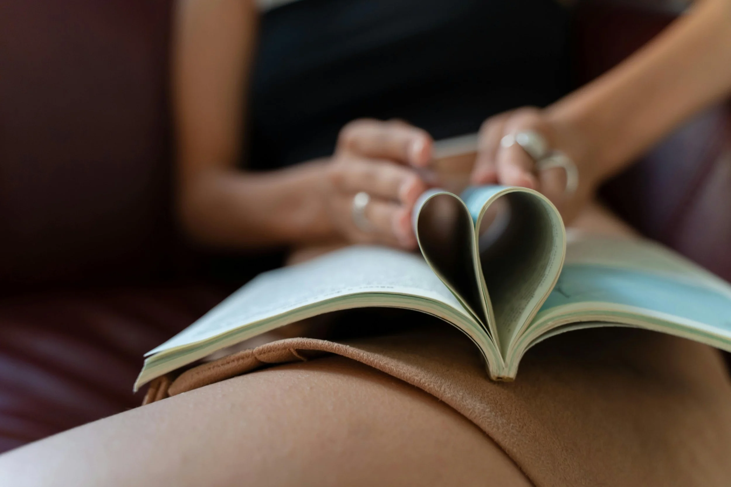 A person sitting with a book in their lap, the pages of the book folded to form a heart shape. to signify Dithering Chaps approach to publishing poetry chapbooks