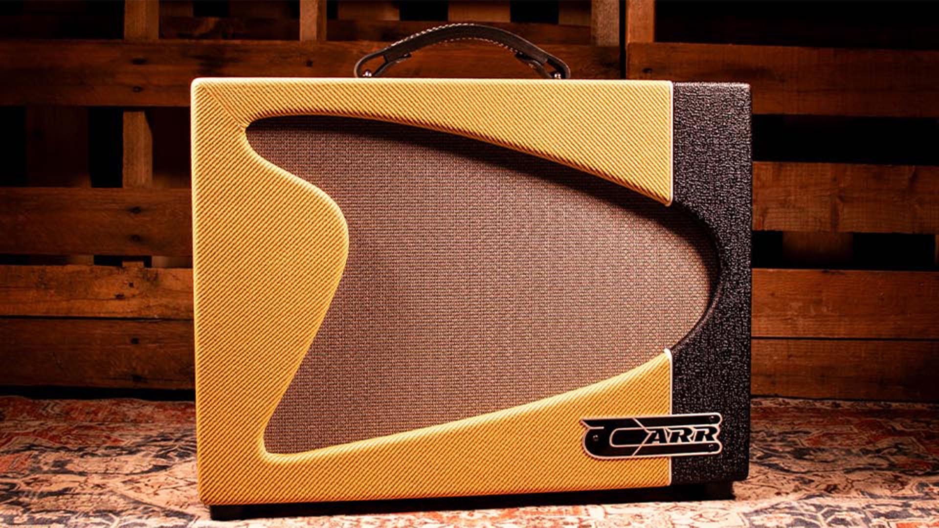Close-up of a yellow and black guitar amplifier with a textured grille and a handle on top, placed on a patterned rug with a wooden wall background.