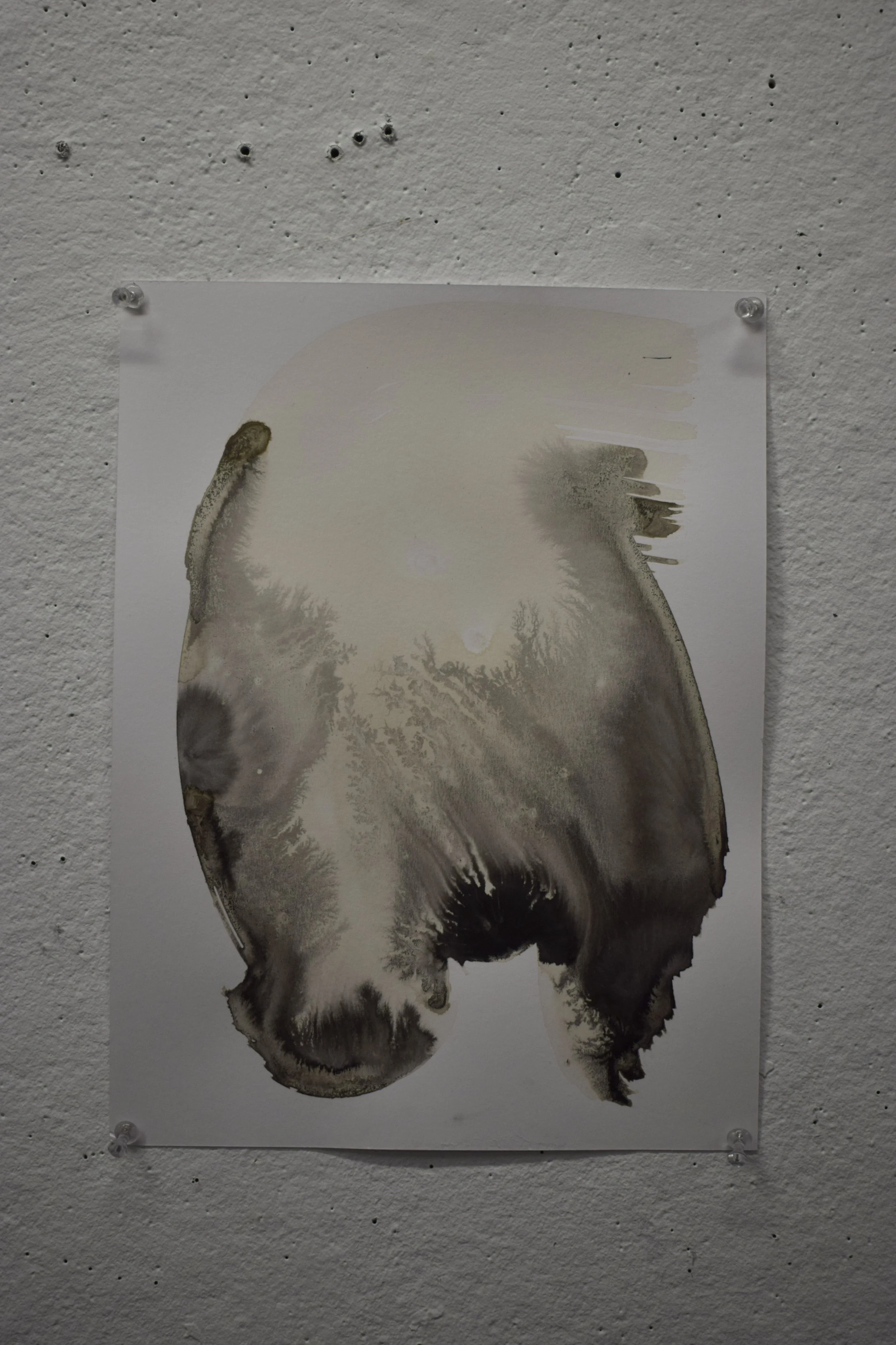 Abstract black and beige ink splatter on white paper pinned to textured white wall.