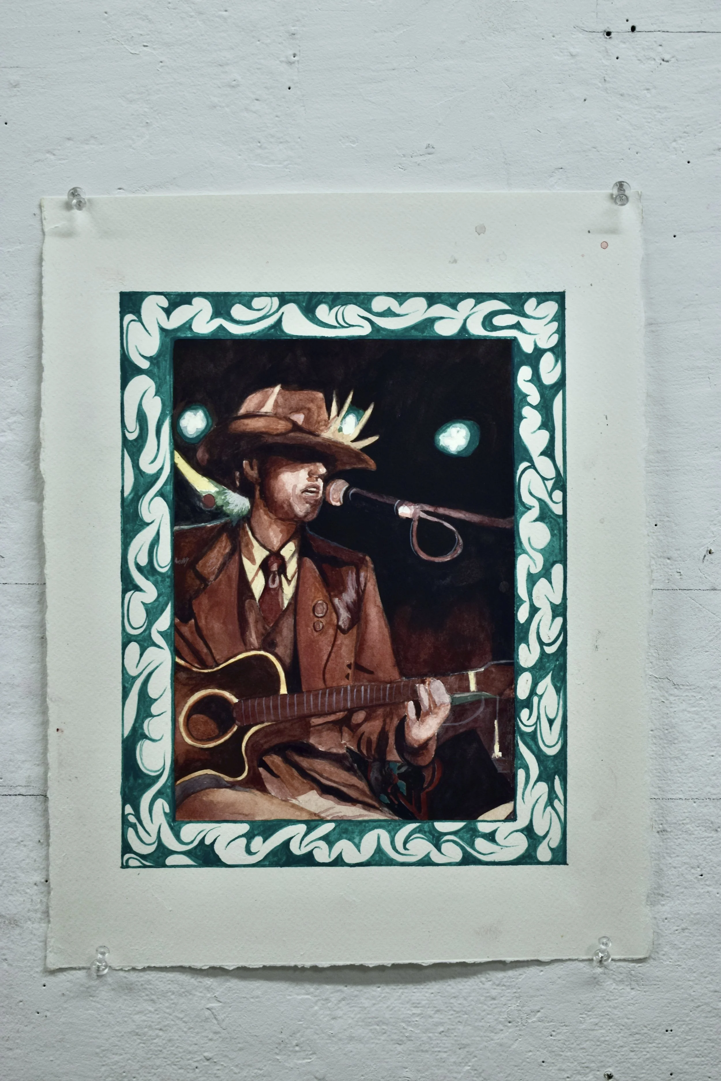 Painting of a man wearing a cowboy hat and brown jacket, playing an acoustic guitar and singing into a microphone, framed with a decorative teal border.
