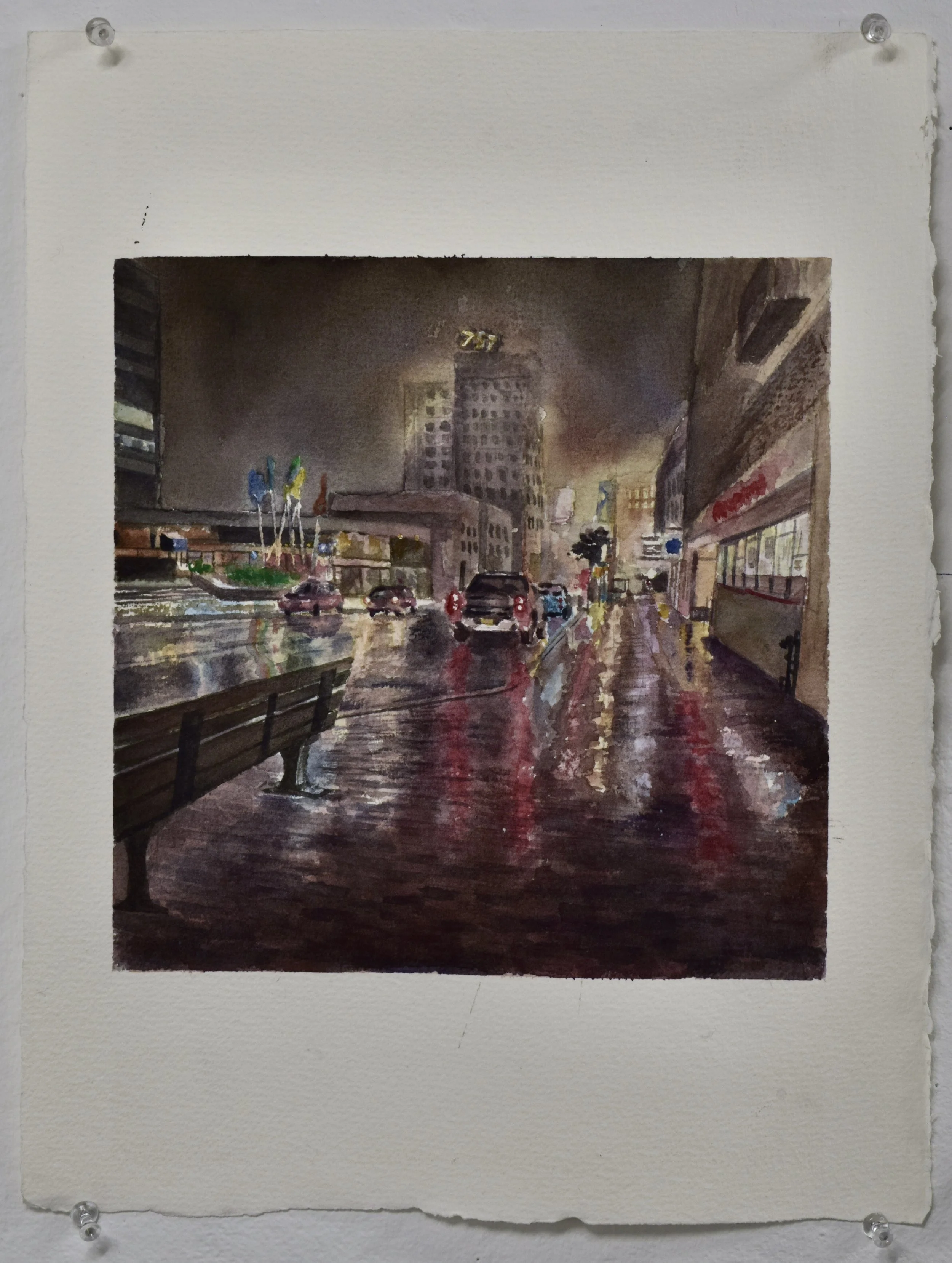A watercolor painting of a city street scene at night with wet pavement reflecting lights, parked cars, tall buildings, and a row of flagpoles with flags.