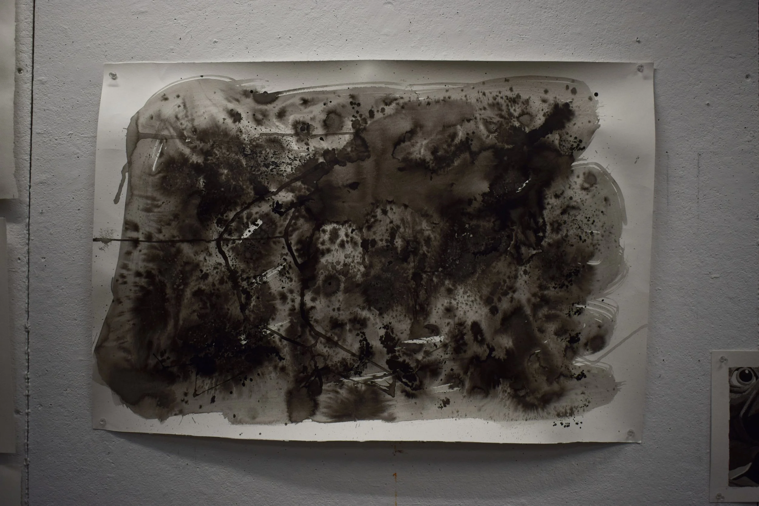 Abstract black and gray ink blot painting on white paper mounted on a white wall.