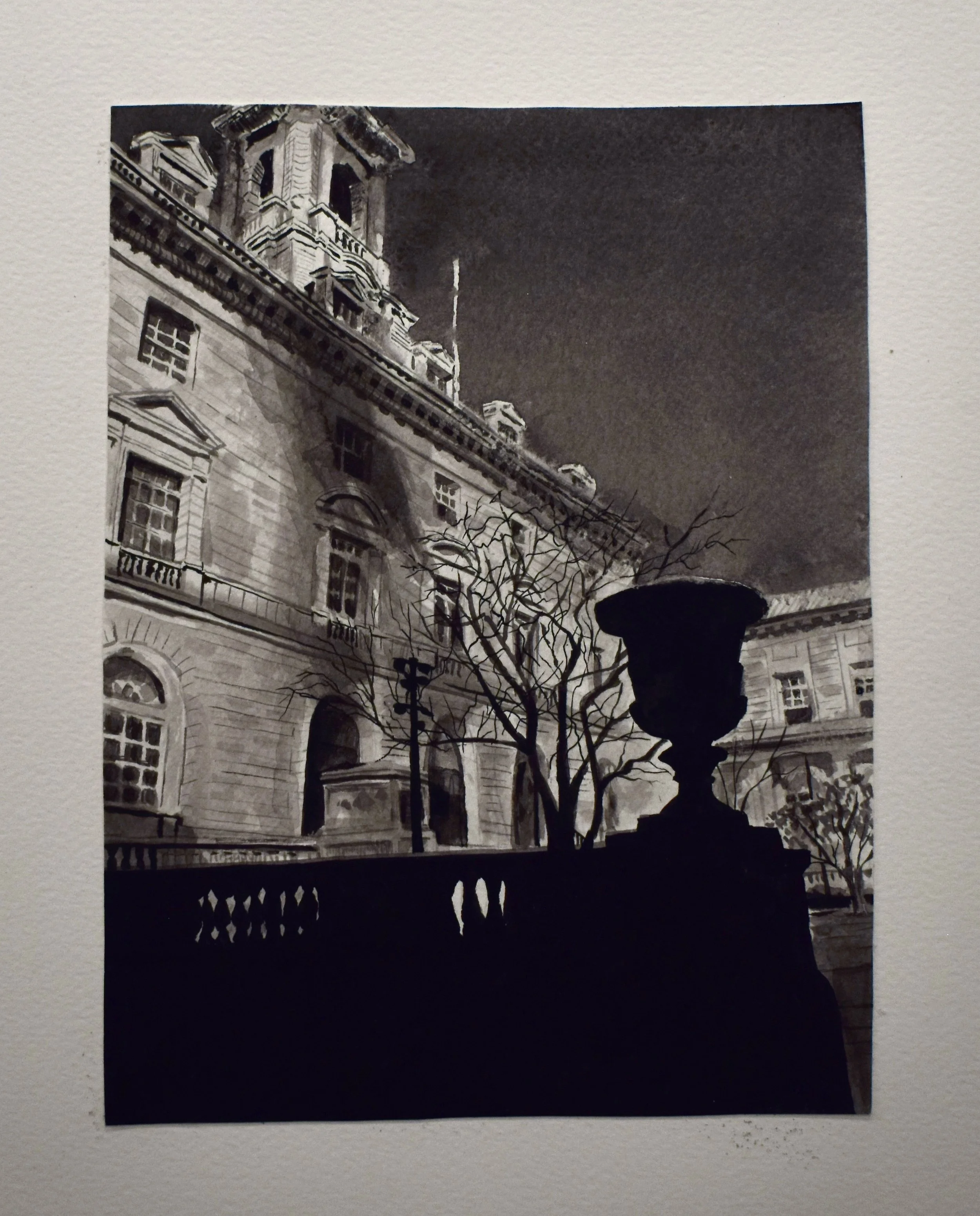 Black and white photograph of a historic building at night with lit windows, a bare tree, street lamp, and a large decorative urns or planters in silhouette.