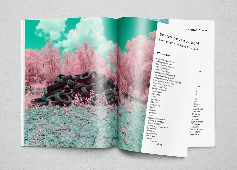 An open magazine laying on a gray surface, showing a two-page spread. The left page has an image of a pile of black tires in an outdoor setting with pink trees and a turquoise sky with clouds. The right page has printed text, including a poem titled "Poetry by Ian Arnold" and a photograph credit to Rhett Pritchard.