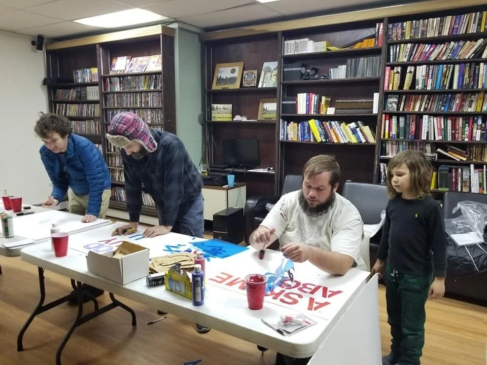 From left to right, Tom Garrett, Patrick Binder, AJ Olding, and Archer Binder make Free Ross signs at the Quill with Lyn Ulbricht.