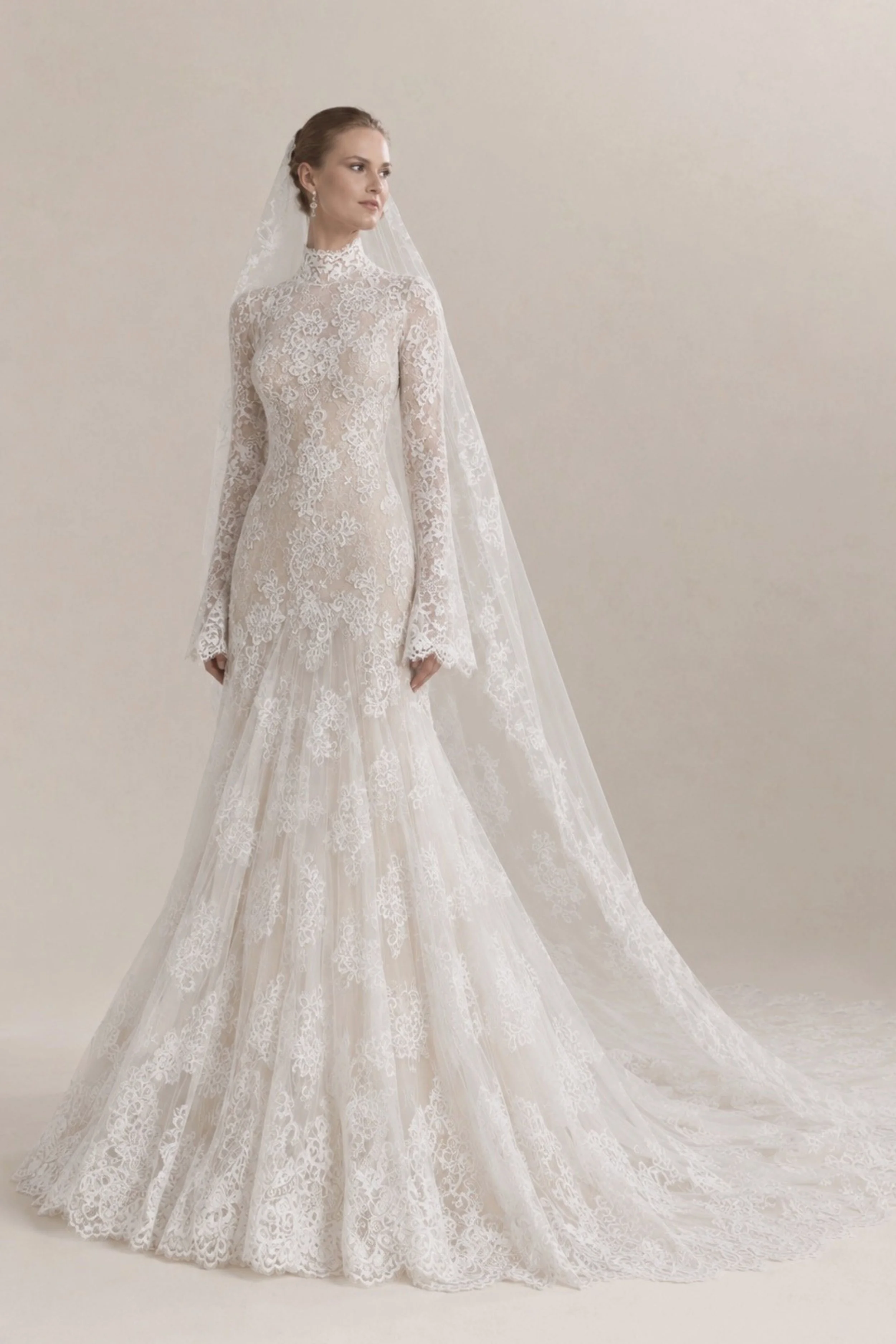 Long sleeve high neck Chantilly lace wedding dress with flared mermaid skirt, scalloped train and cathedral veil for a classic modern bride.
