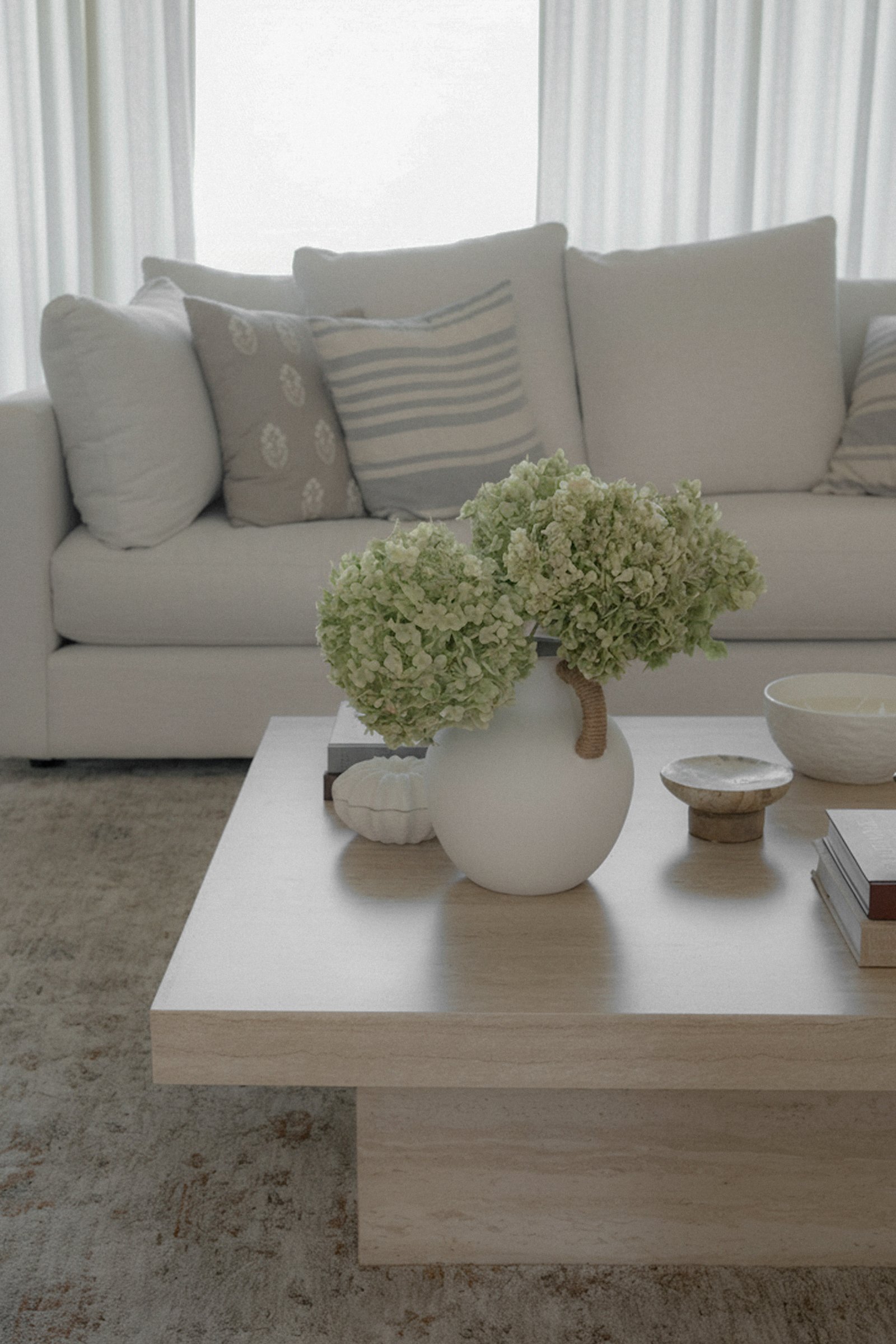 A white sofa with a coffee table in the foreground, with a large vase of flowers on it.