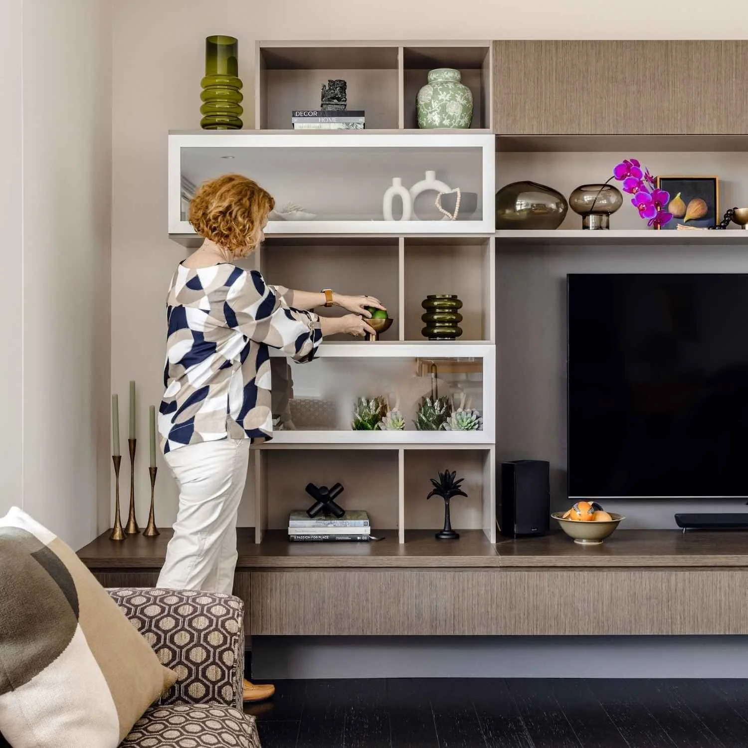 Kate Kerin styling built-in living room shelving with decorative objects, books, ceramics and plants around a television unit.