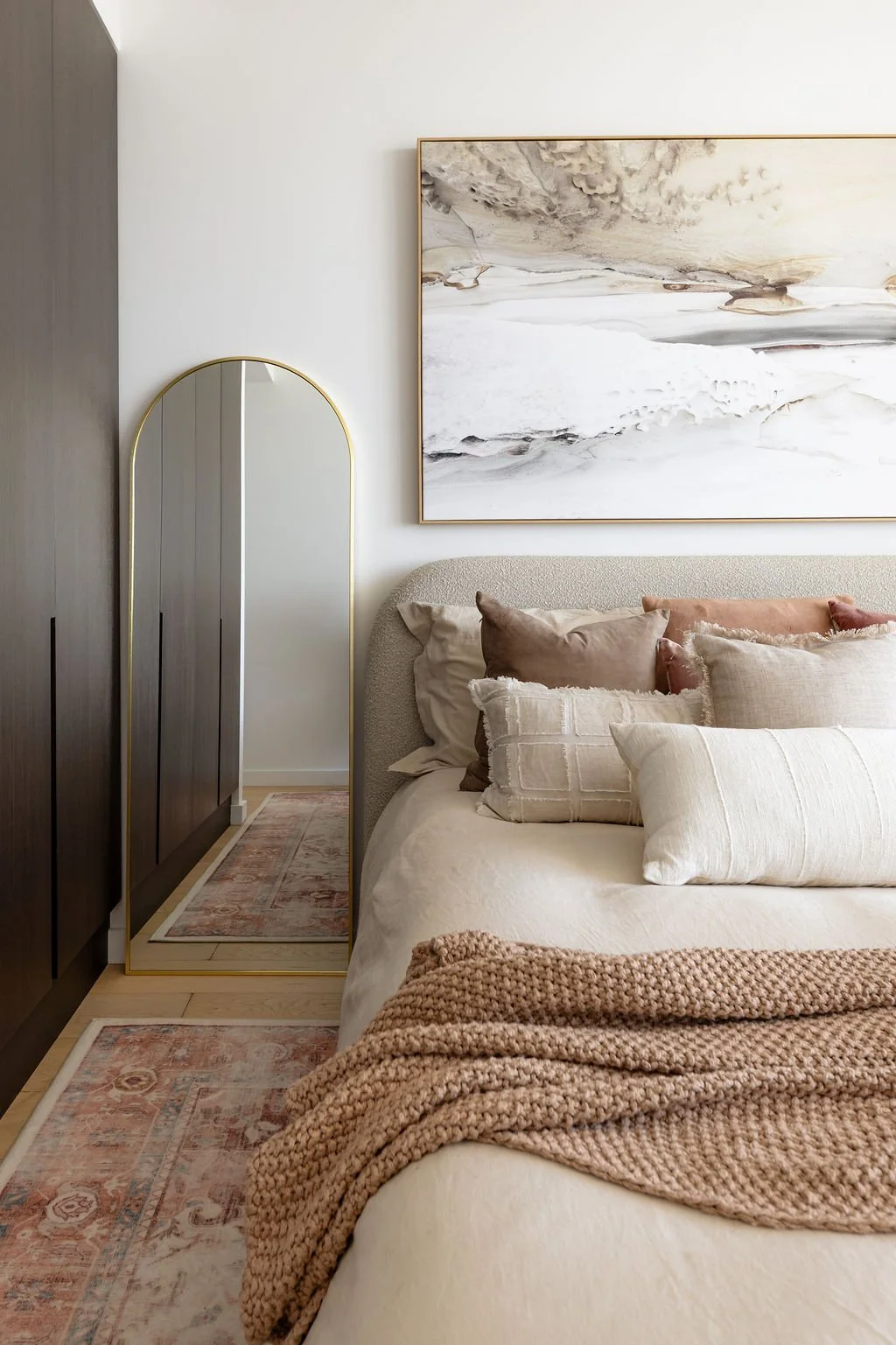 A girl's bedroom with pretty painting above the bed and an arch shaped mirror on the floor.