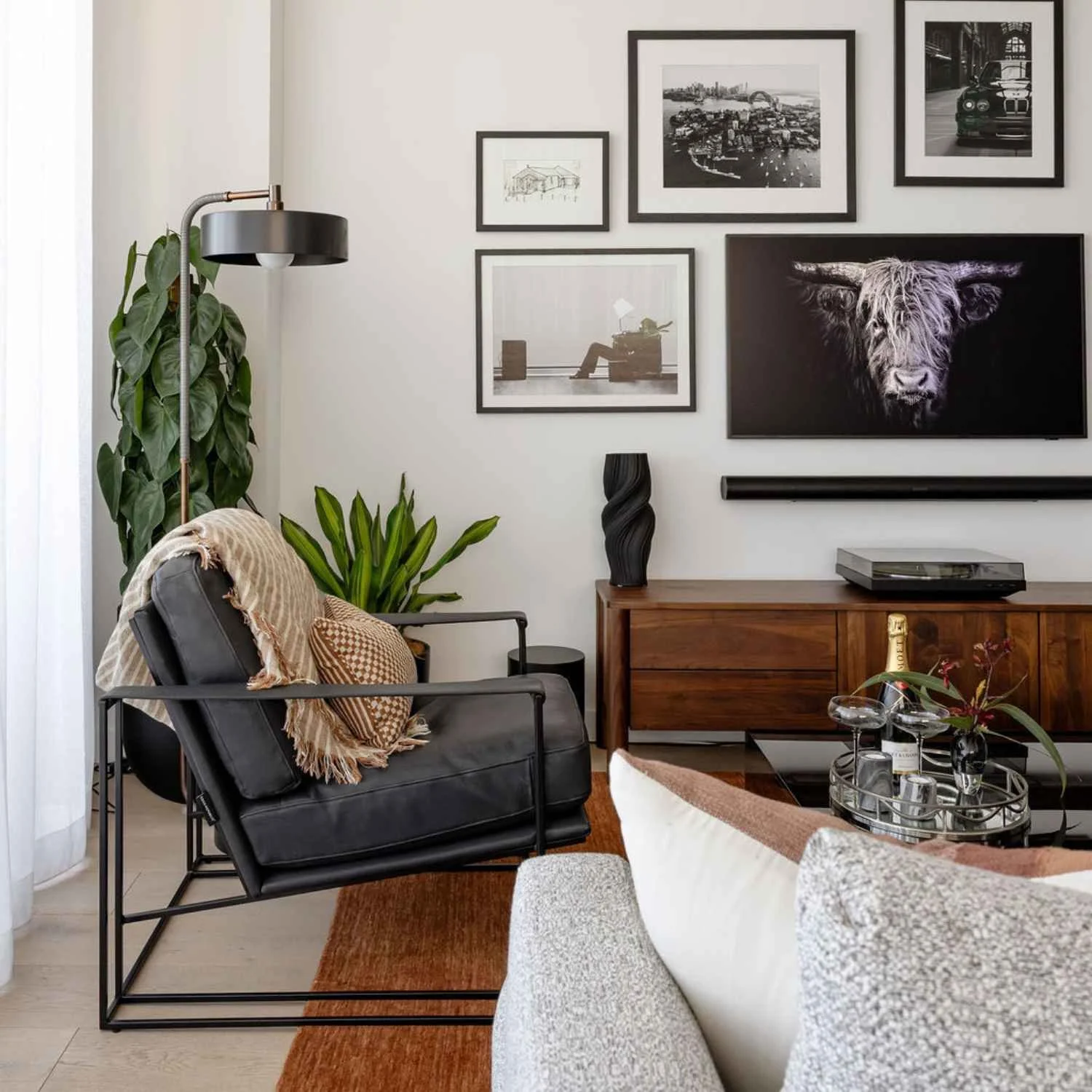 Styled living room with black armchair, timber sideboard, indoor plants, framed artwork and a wall-mounted television.
