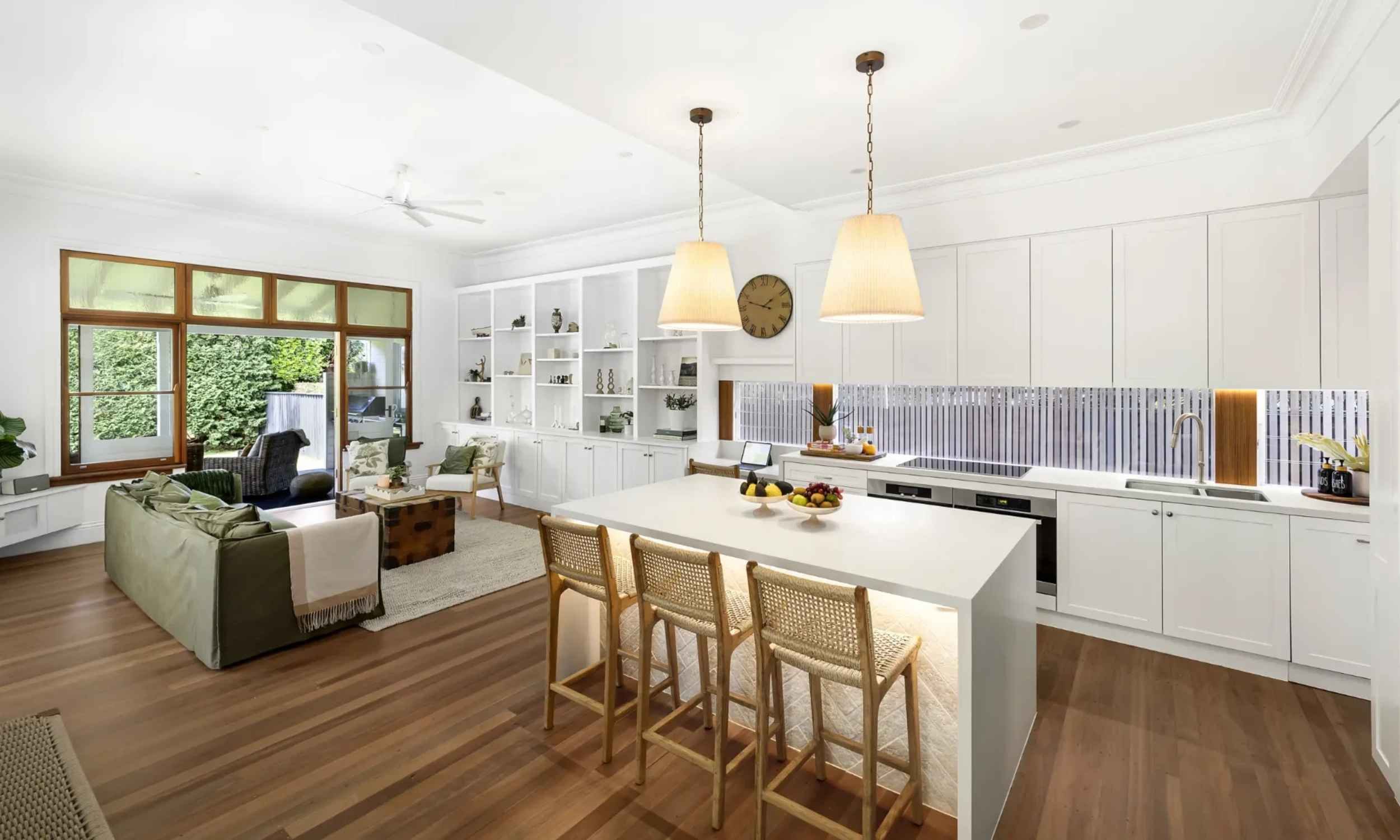 Open-plan Collaroy kitchen and living area with white cabinetry, large island bench, pendant lights, timber flooring and relaxed seating.