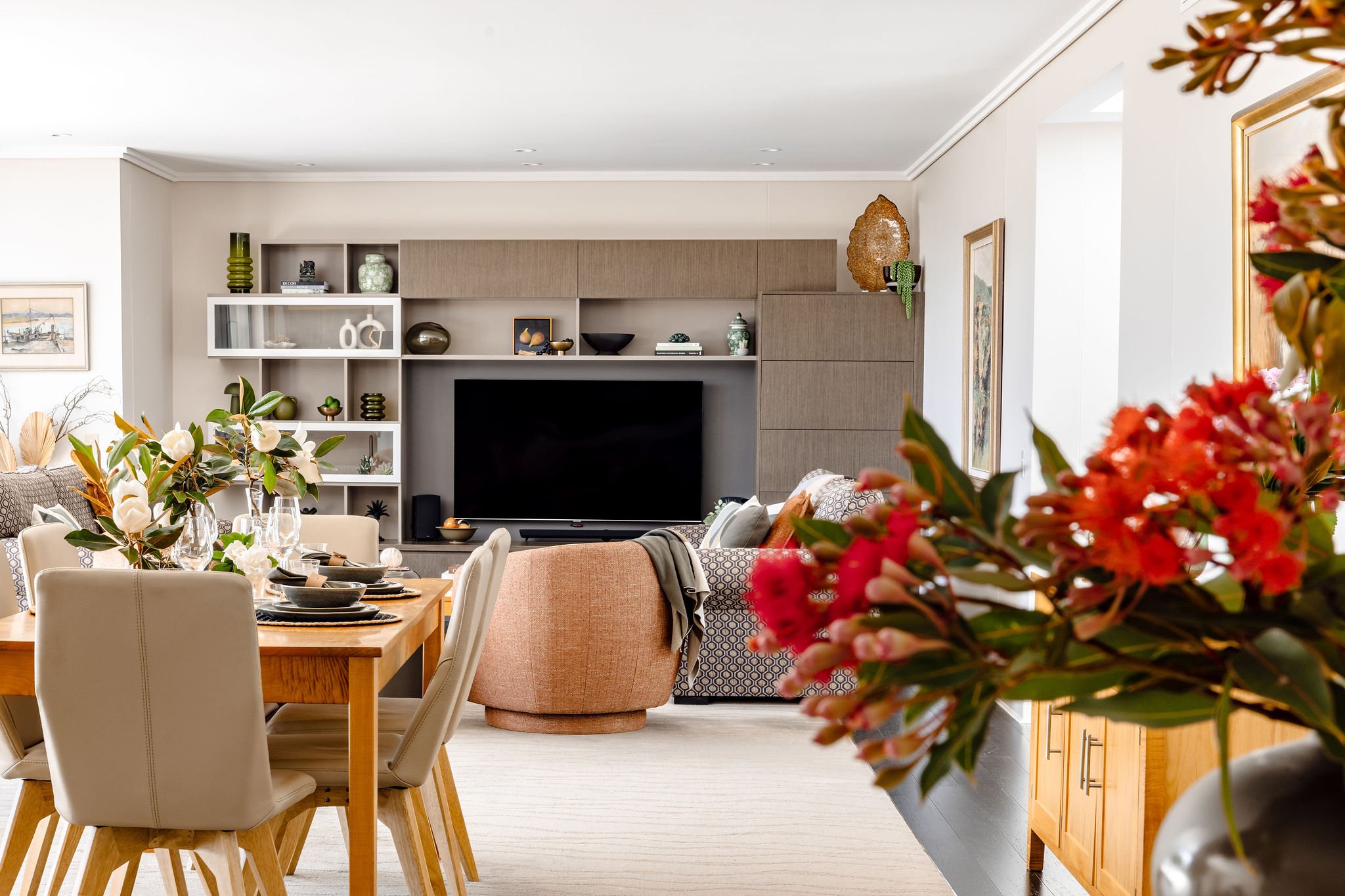 A long view of a dining and living room, with bush flowers in the foreground