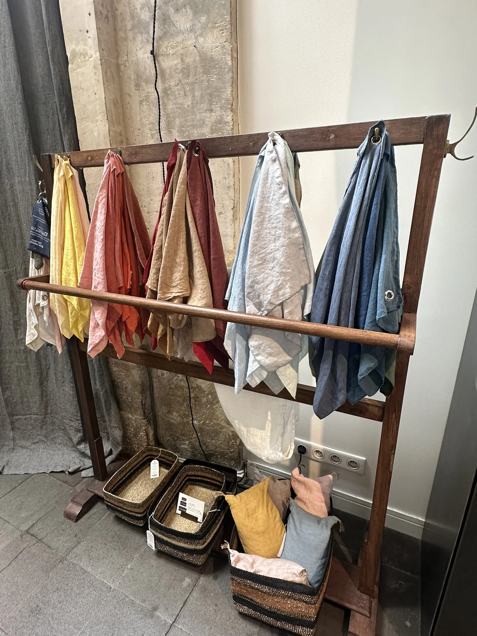 Colourful linen serviettes hanging on a wooden rack, with baskets below.