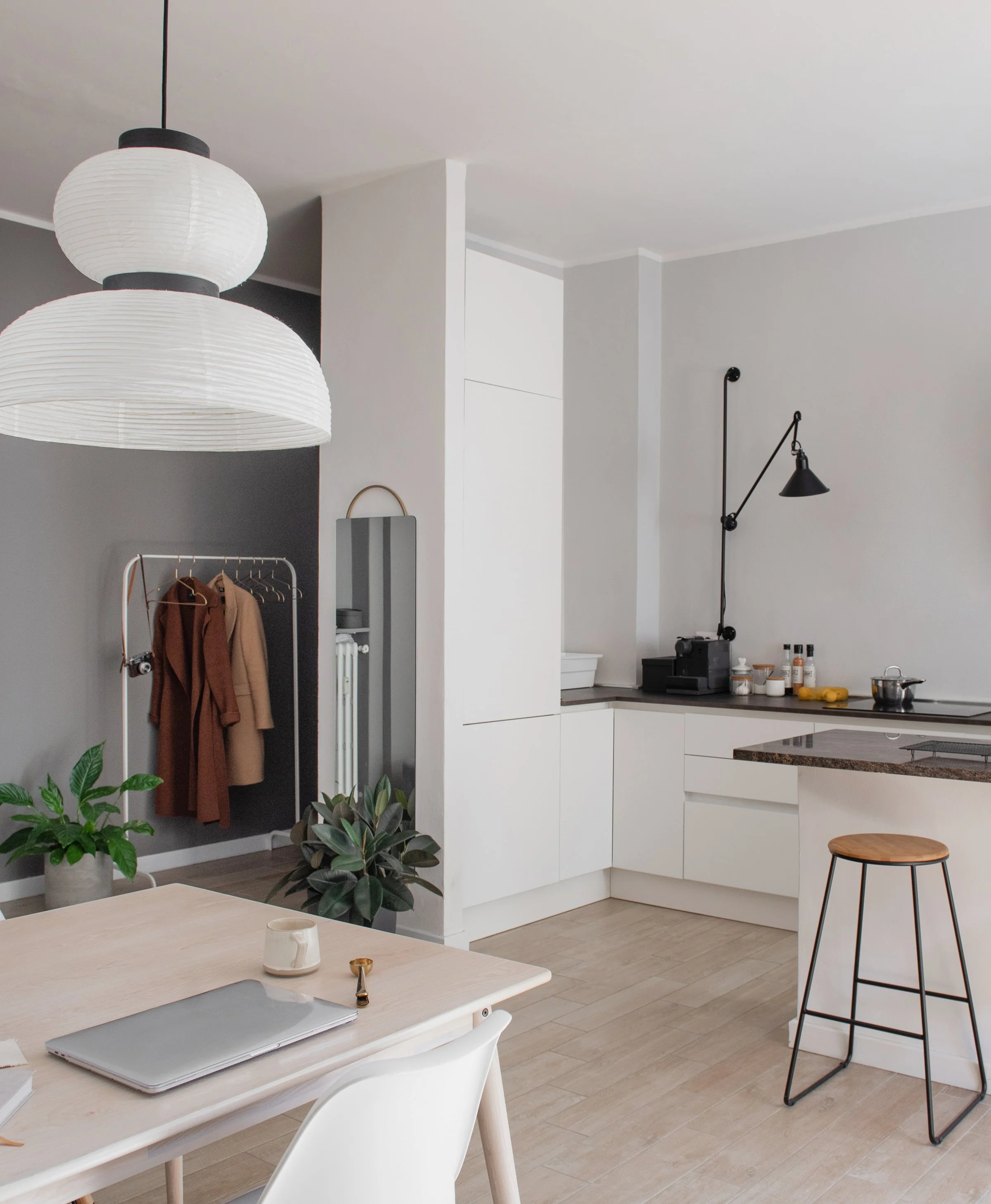 Internal view of an apartment, with a modern light fixture and a coat rack. The kitchen is in the background.
