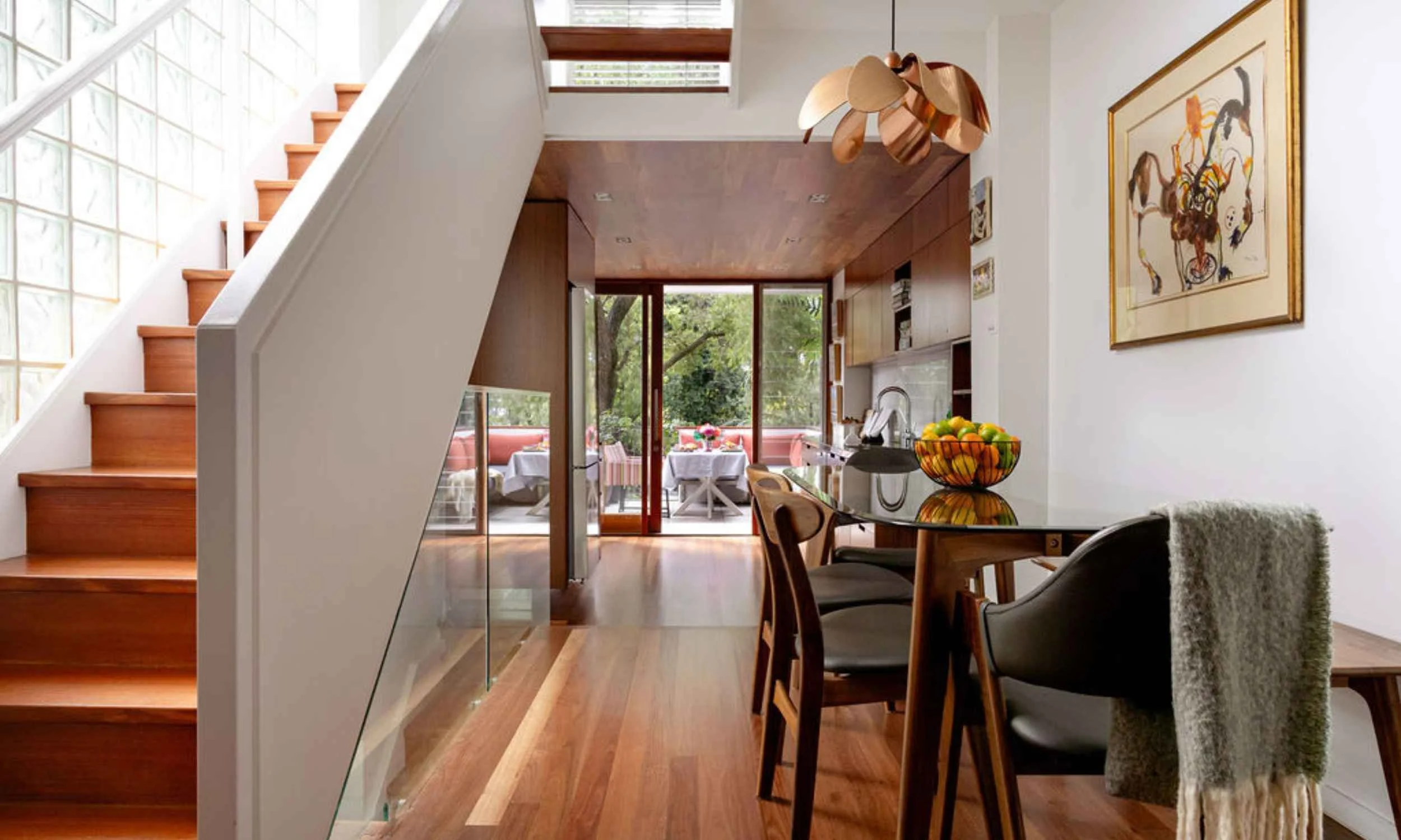 Birchgrove home interior with timber staircase, dining area looking through to the outdoors, warm timber flooring and a dining nook with overhead pendant light and fruit bowl on the table..