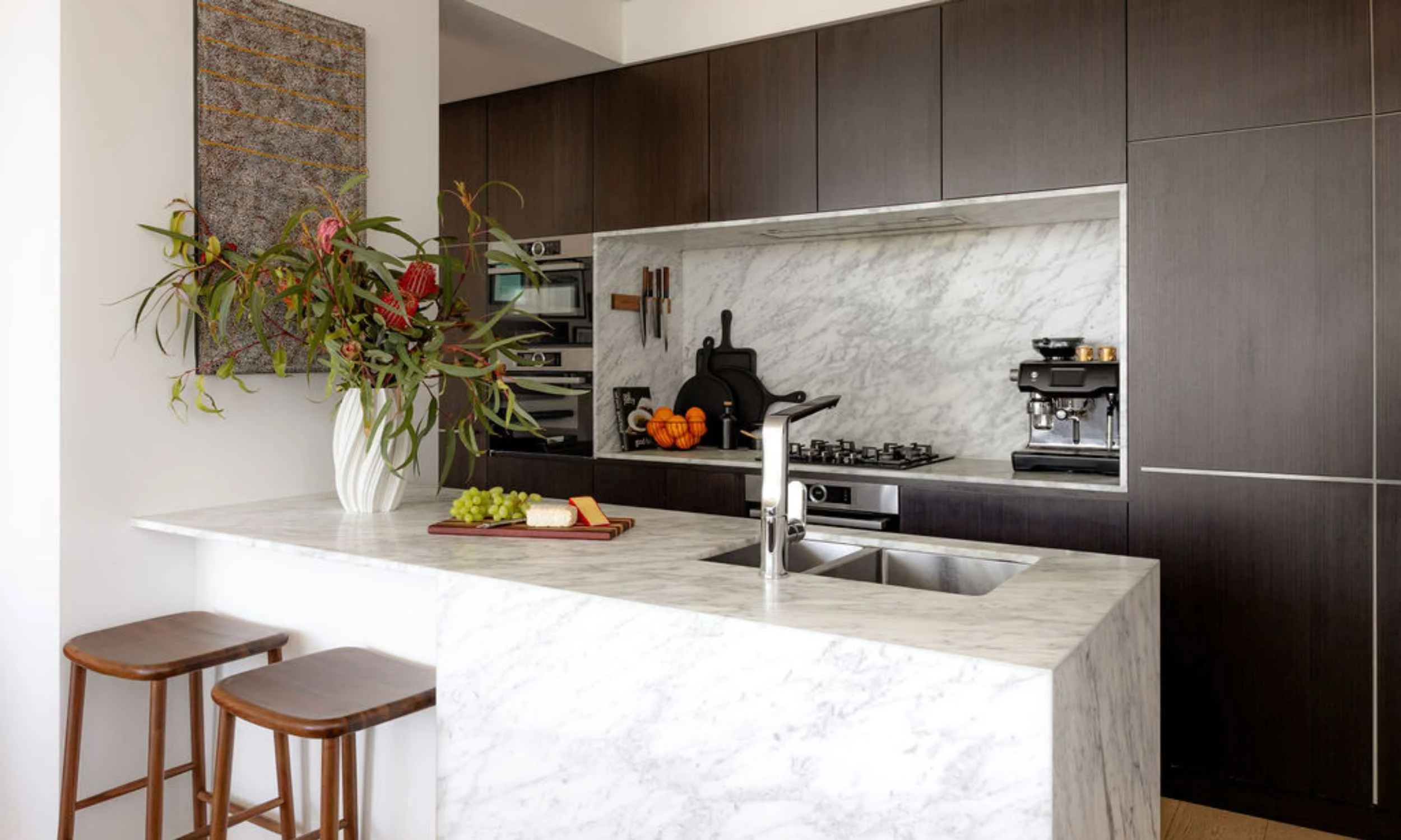 Contemporary North Sydney kitchen with dark timber cabinetry, marble splashback and island bench, styled with flowers and serving pieces.