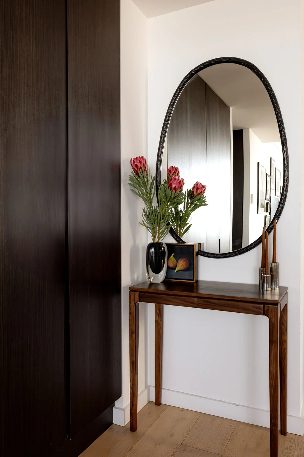 A foyer area with large sculptural mirror and dark cupboard doors.