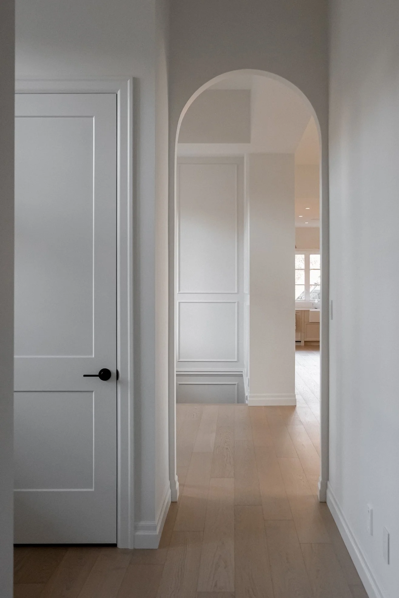 A hallway with arched door, lovely white walls and light oak floor boards