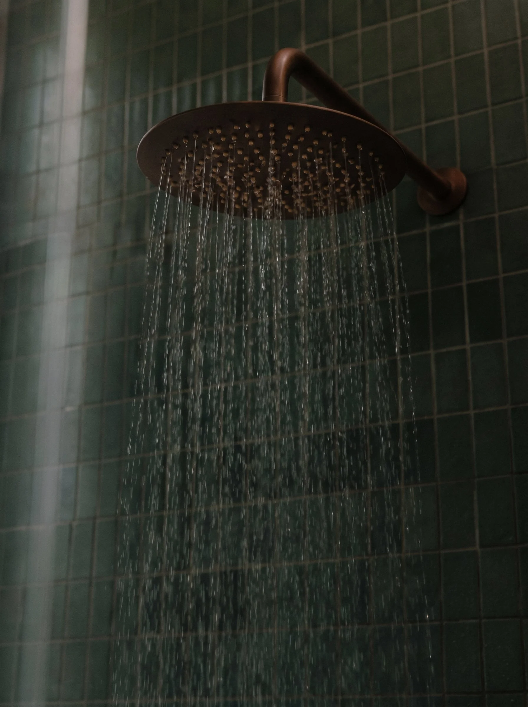 An image of a rain head shower with moody dark tiles behind it.