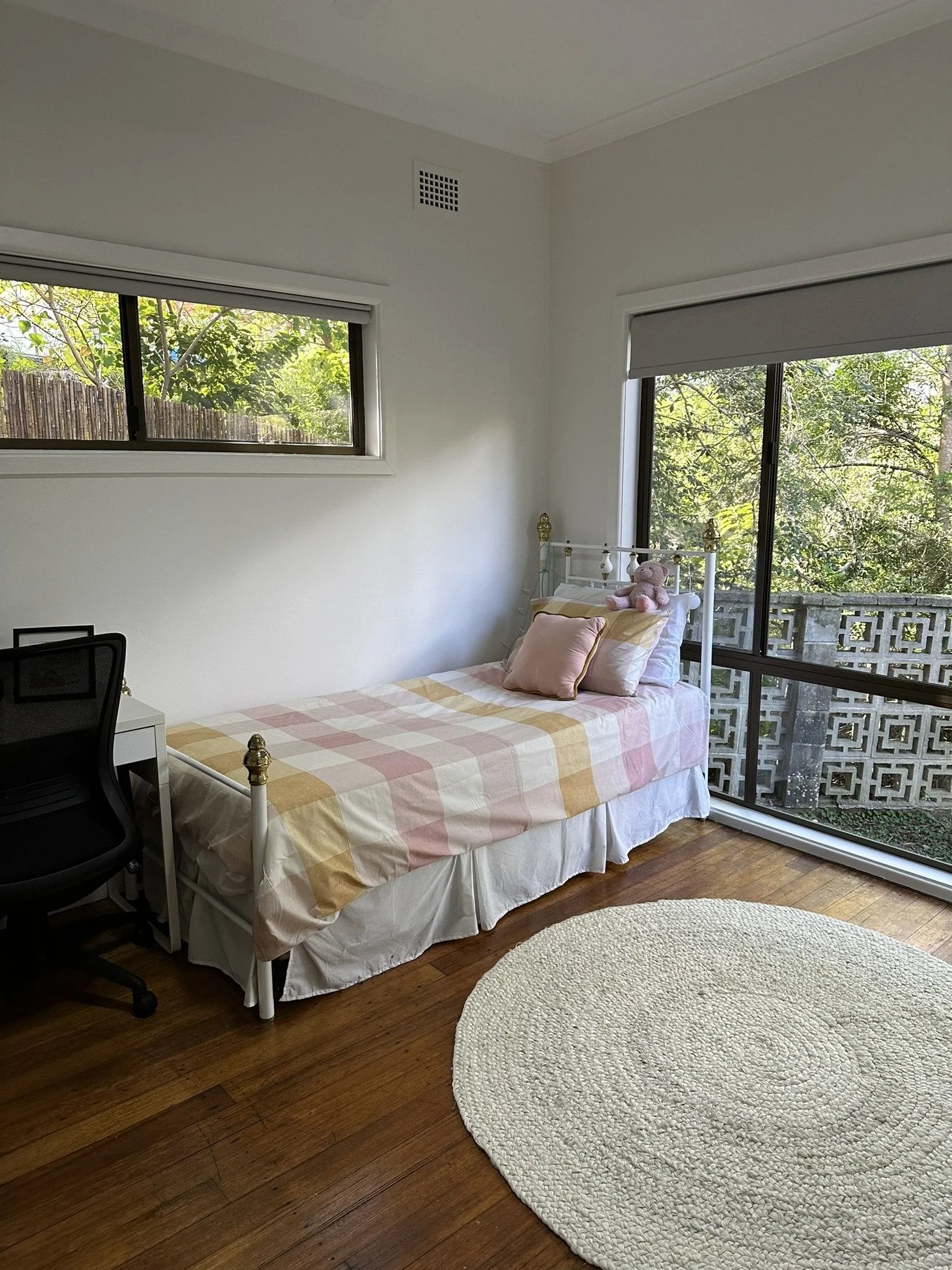 A pretty girl's bedroom with round rug on the floor, pink checked bedspread and windows all round.