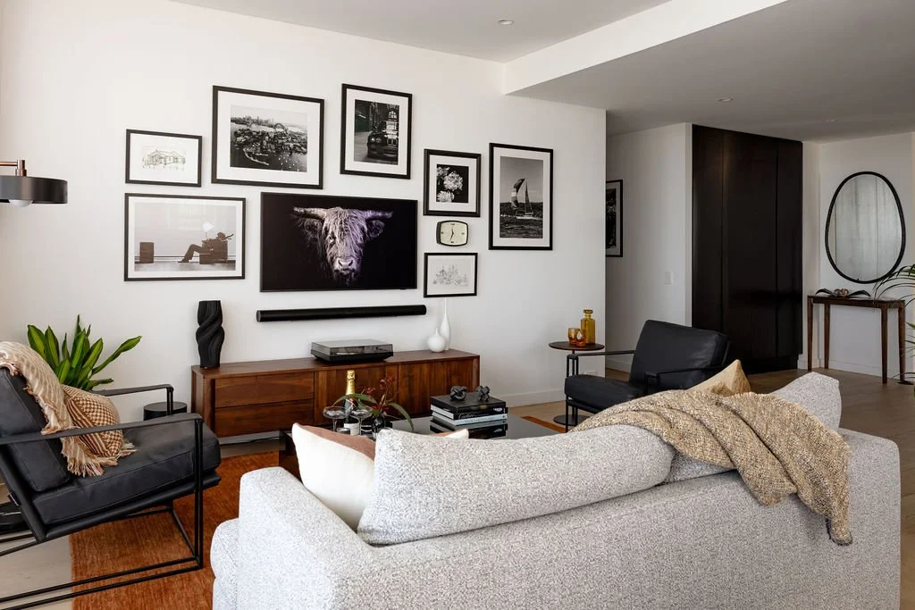 Living room with easy chair, sofa and a gallery hang wall with TV above a mid century style TV unit.