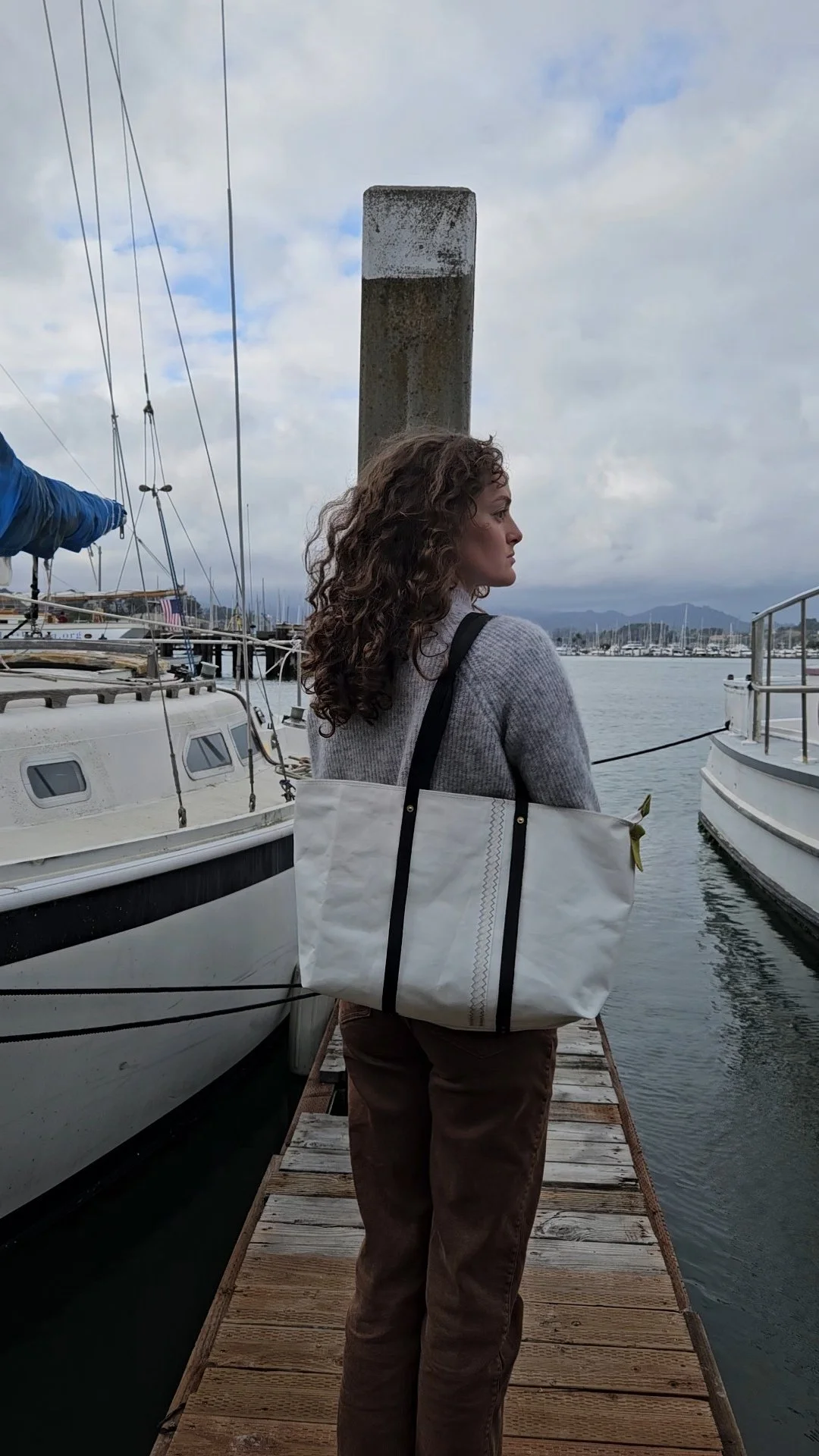 Girl standing on dock wearing bag made from old sails on her shoulder.