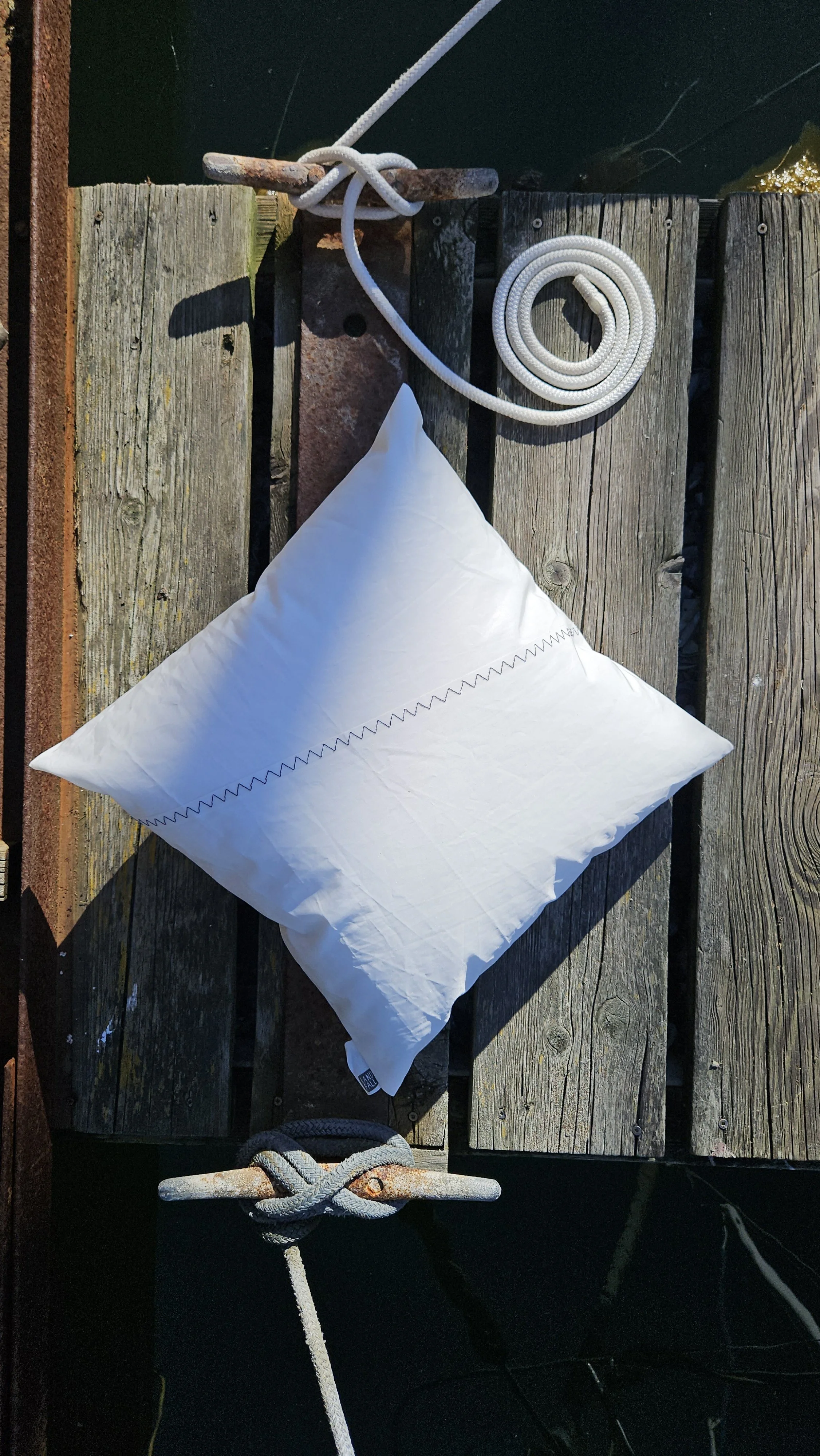 Upcycled sailcloth outdoor pillow made from reclaimed white sailcloth with nautical stitching, designed for coastal patio decor