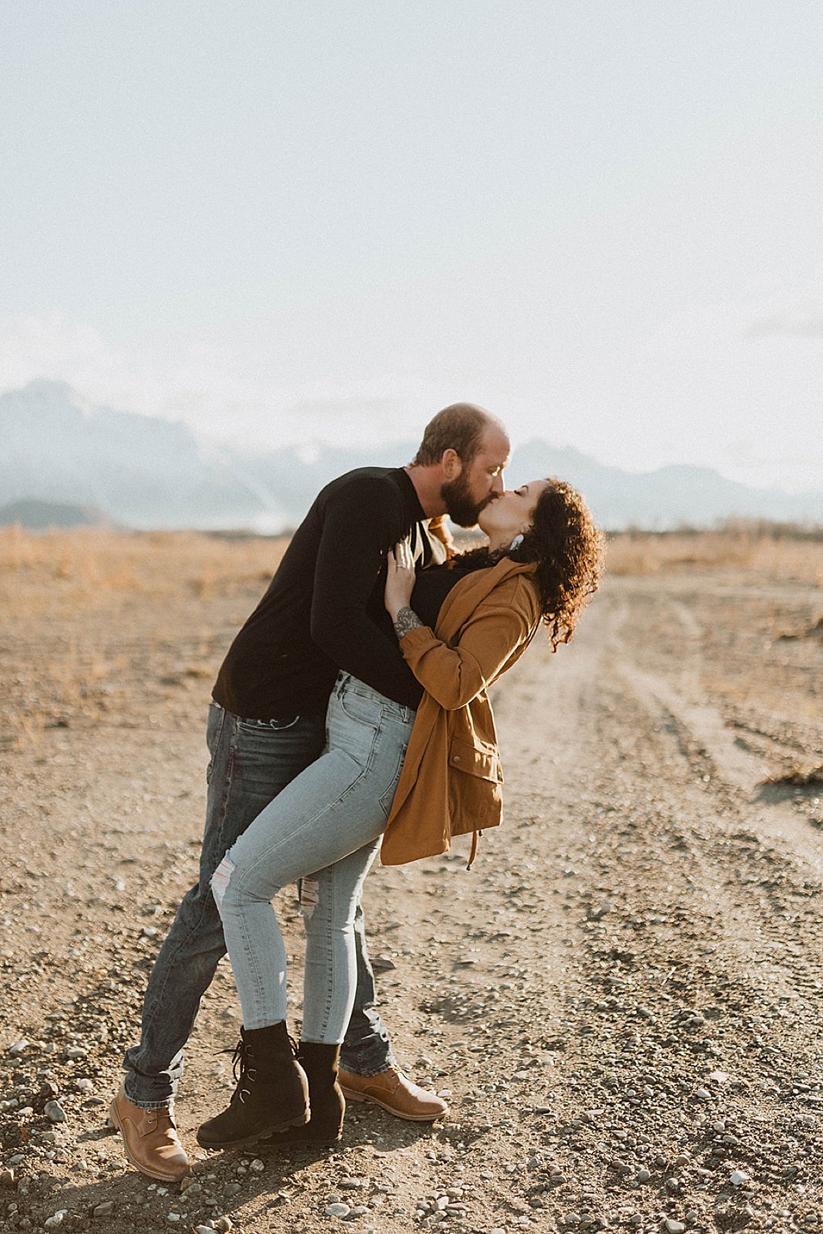  Couple kiss during warm sunset engagement shoot in Alaska mountain park 