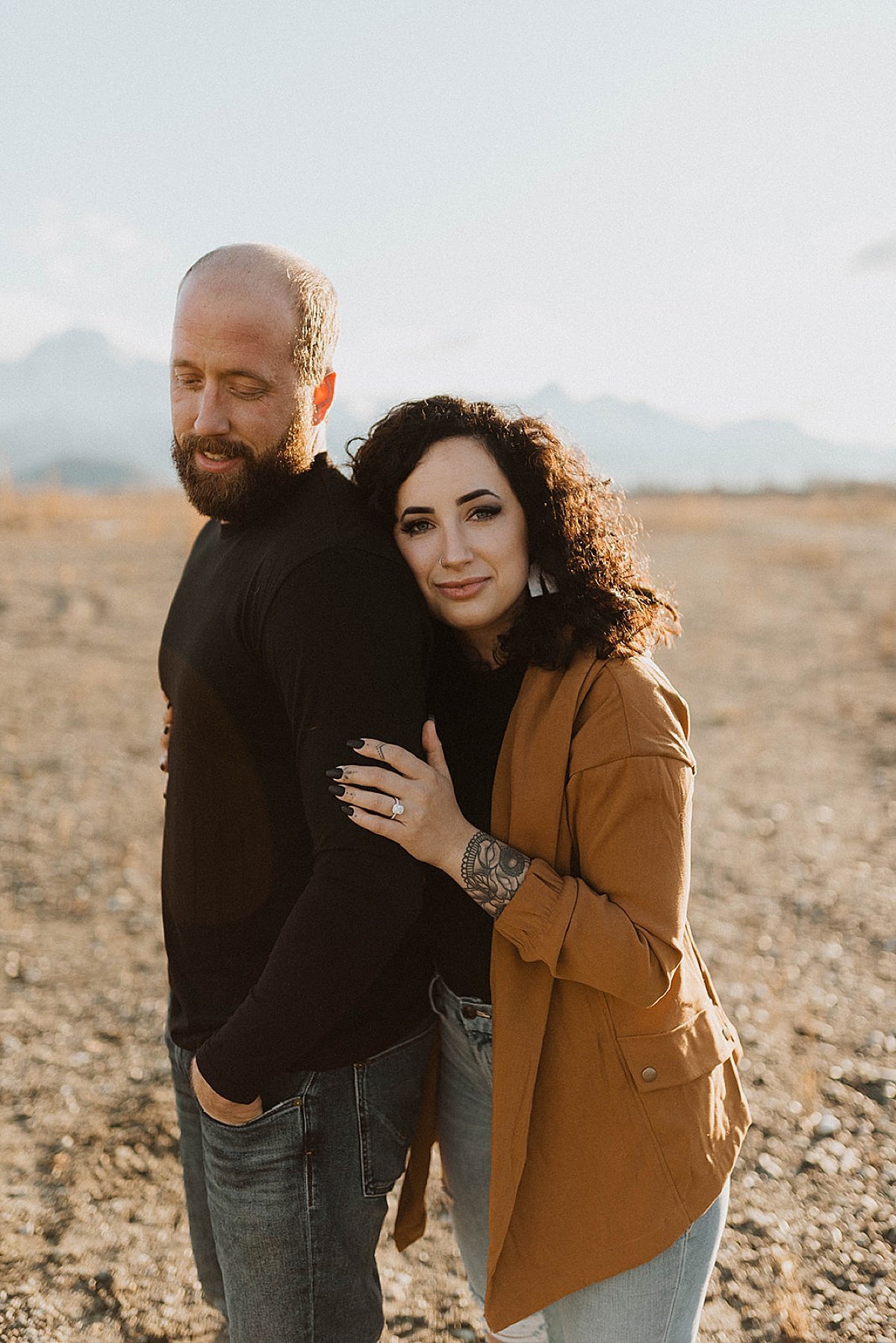  Man and woman embrace during warm sunset engagement shoot in alaska mountain park  